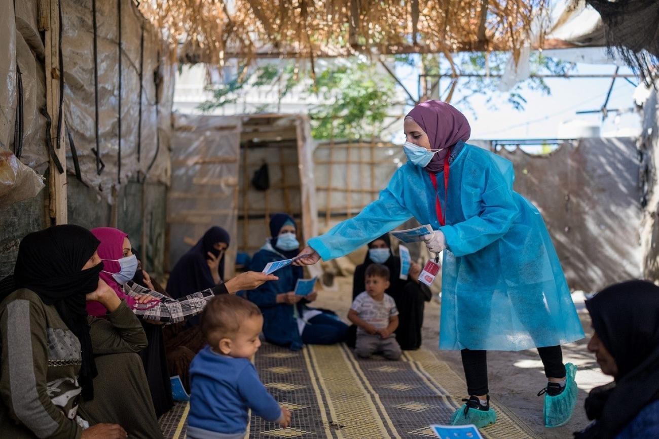 A woman in protective gear hands out a pamphlet to women and children.