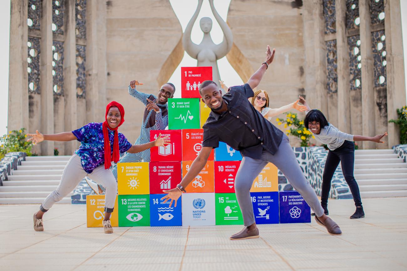 Four children playfully stand in front of a series of block with the SDGs