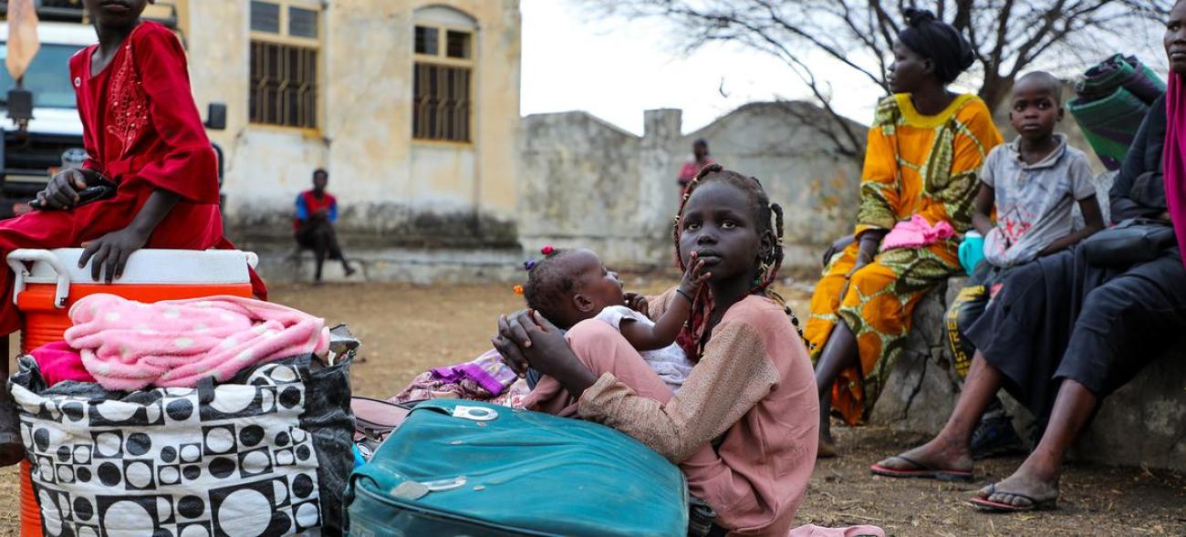 A group of people from Sudan sitting on the ground, the woman at the center is in a pink dress hold