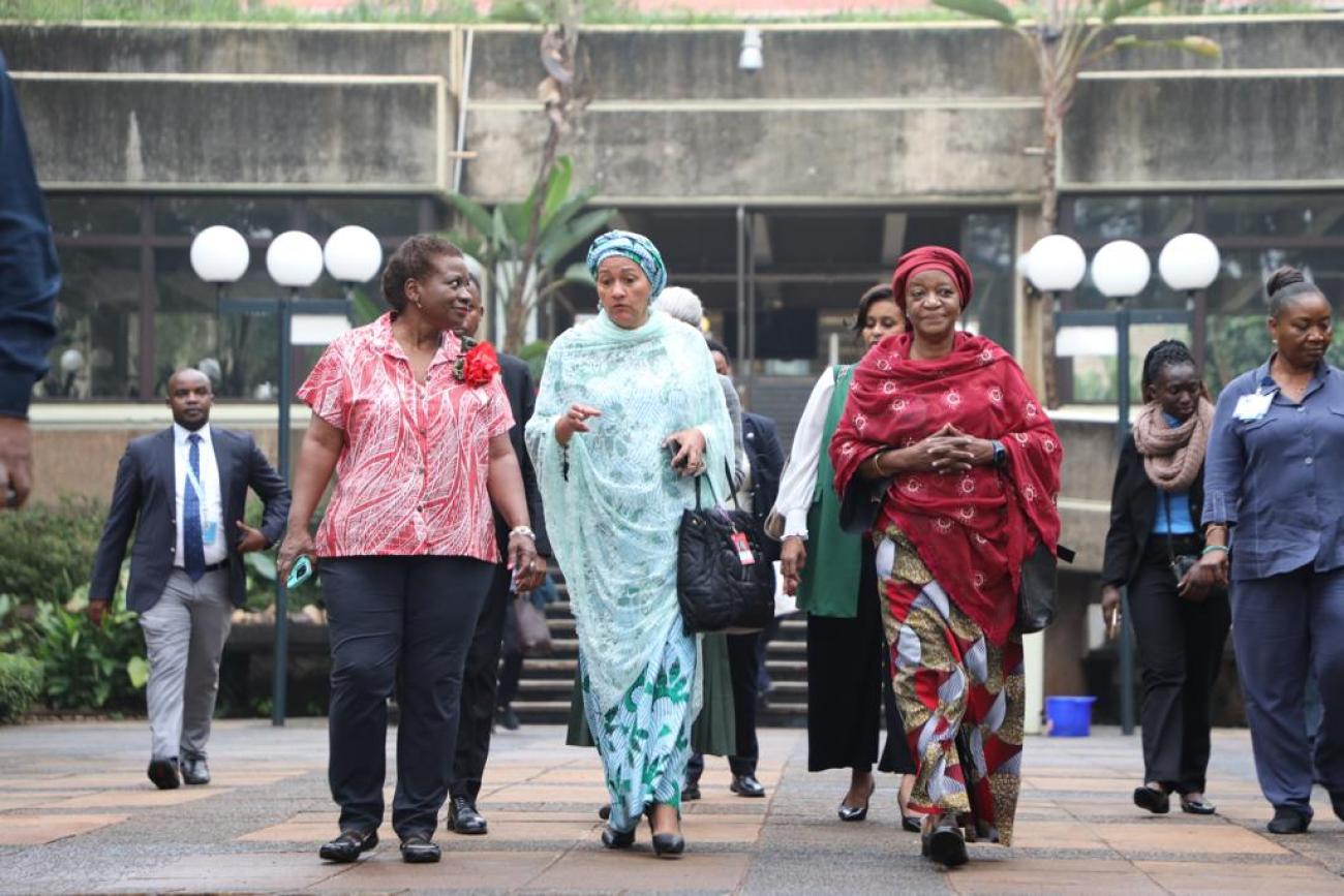 Woman in a blue dress walking and flanked by others around her in a grey stone building