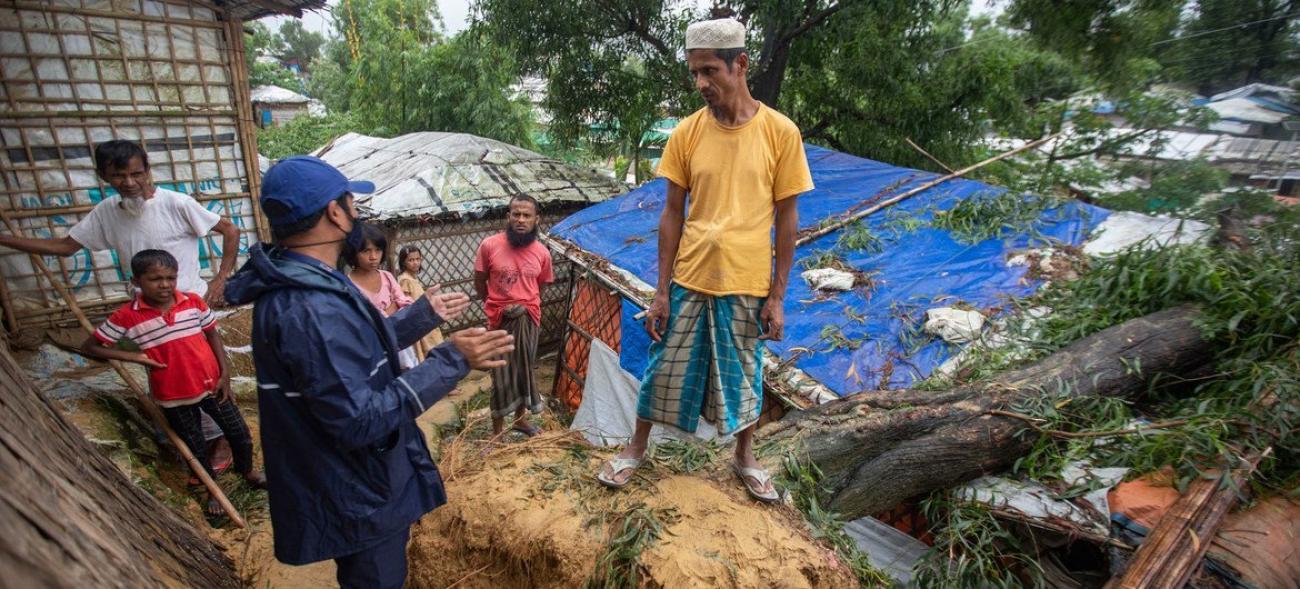 Group of people including two children gather around some rubble and blue tarpaulin