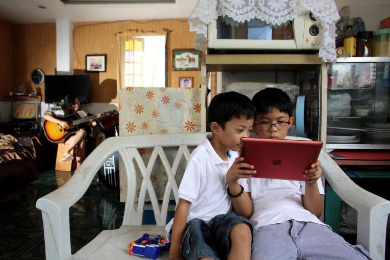 Two children in the Philippines wearing white dresses are crouched over a digital tablet screen