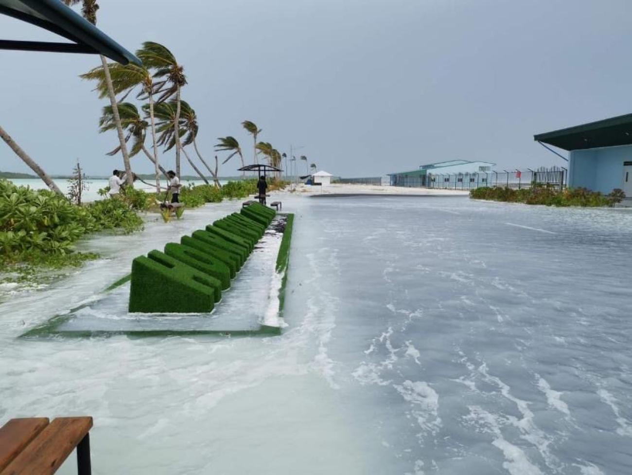 A scene of a beach in Maldives with water pooling by the shore where a green display stands.