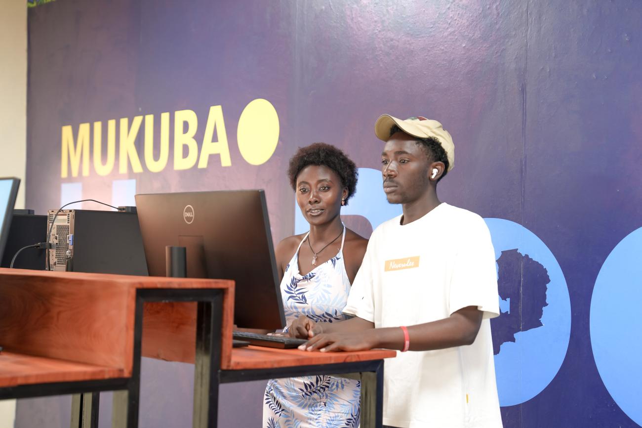 A man and a woman wearing white stand at a desk with a computer in front of them