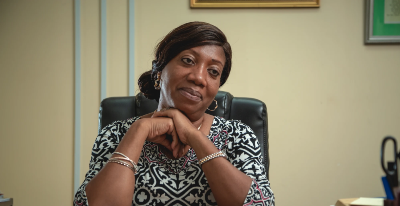 A woman in a black and white blouse sits at a desk with her arms crossed.