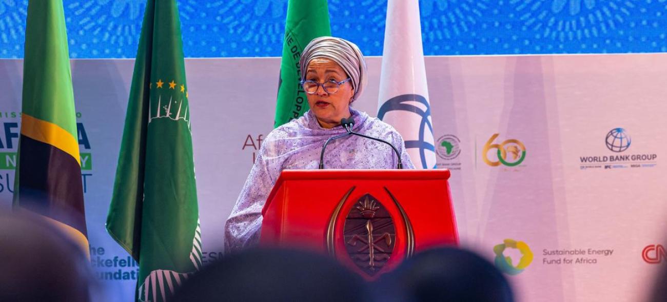 A woman in a purple dress and headscarf, the UN Deputy Secretary-General, Amina Mohammed speaks at a podium against a colourful background