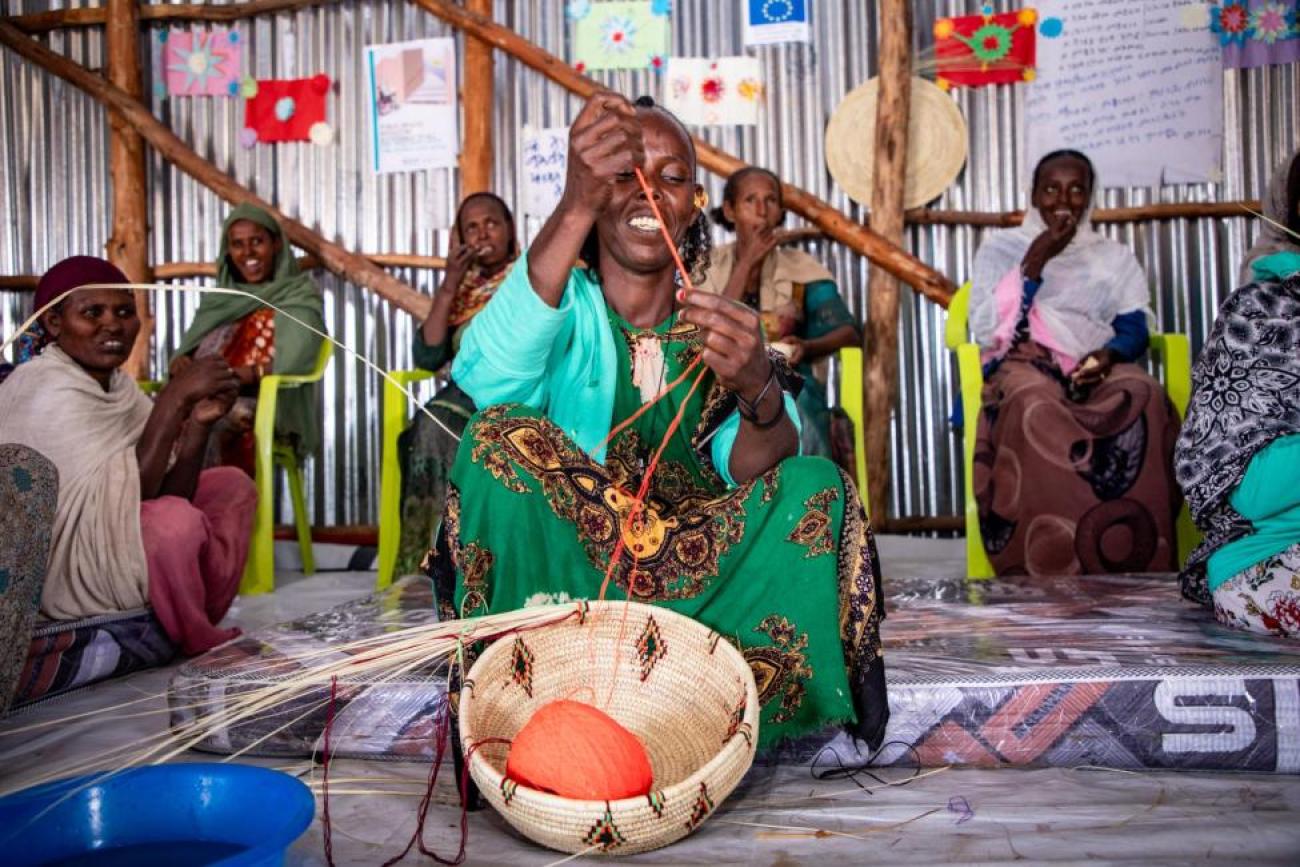 A group of women in colorful traditional clothing are gathered in a circle weaving.