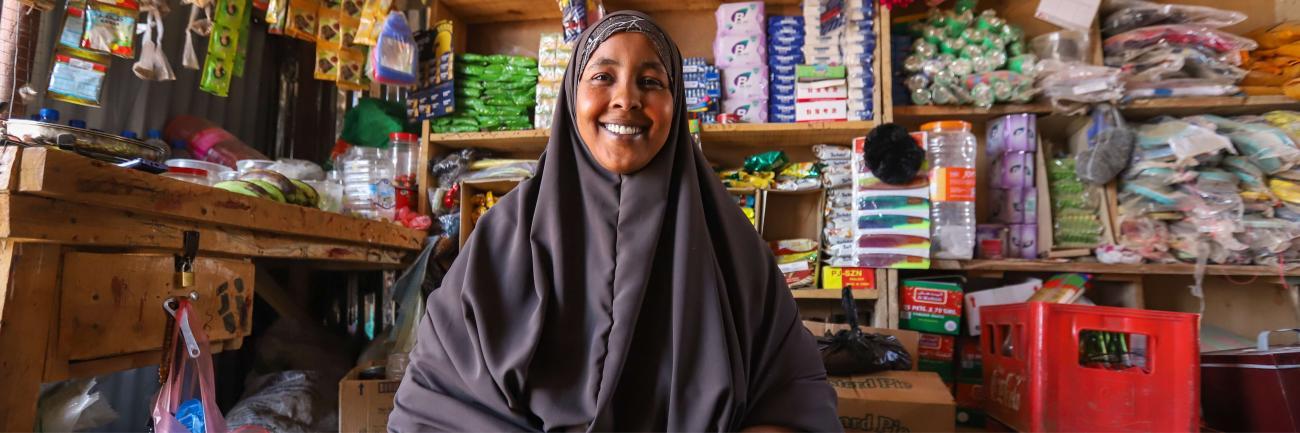 A woman is looking at the camera and smiling and behind her is a shop front