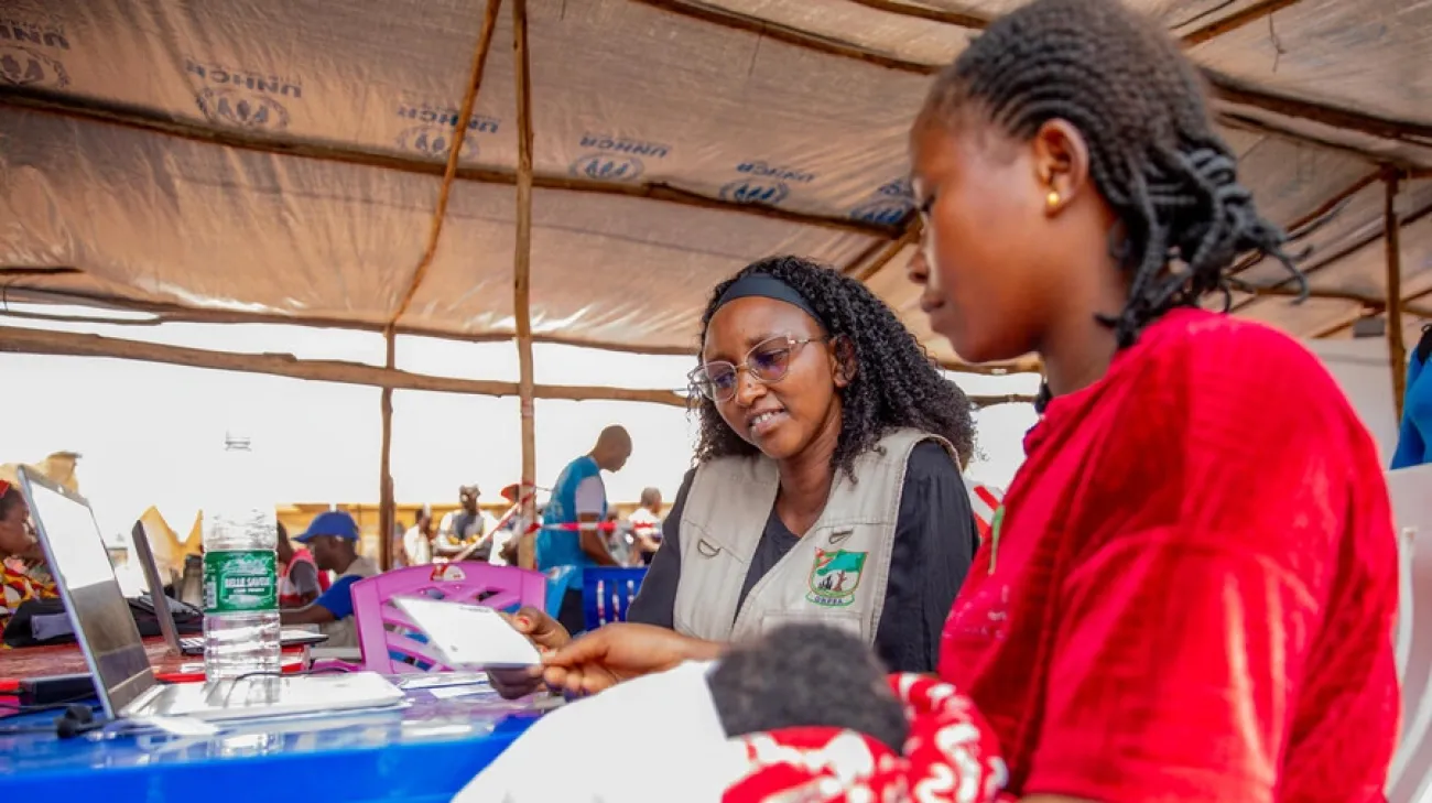 Chancelline regarde sa carte d'enregistrement en tenant son bébé dans ses bras dans un centre d'enregistrement du HCR à Rugombo, dans la province de Cibitoke, au Burundi. 