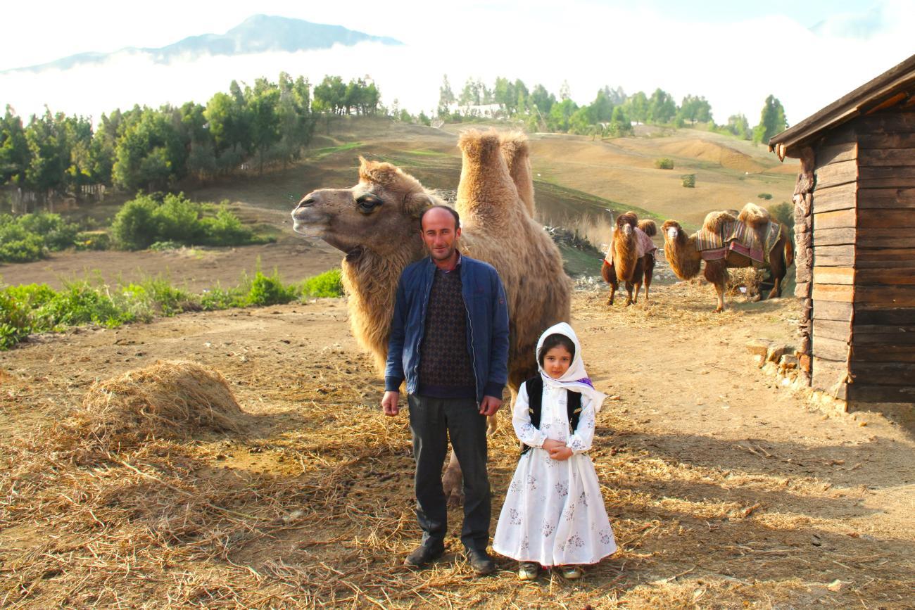 A man with his daughter with a camel in the background