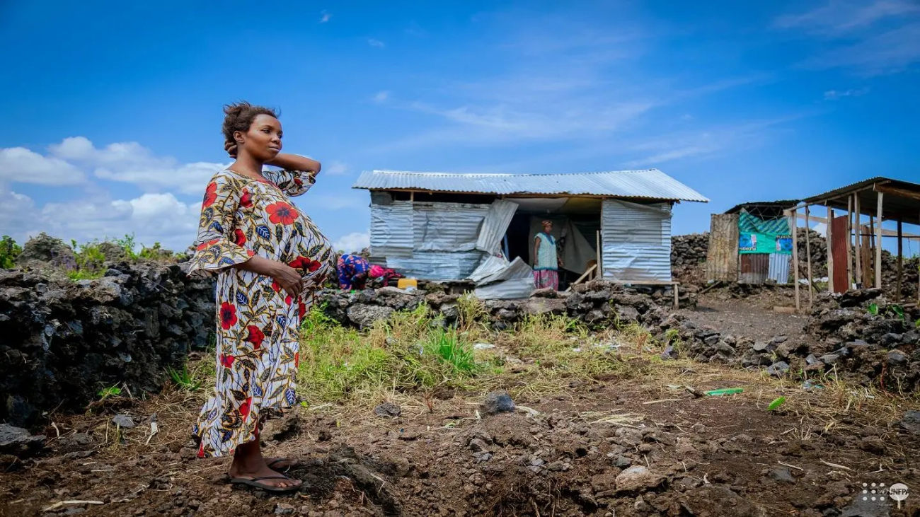 أومبيني مبورانو، حامل في شهرها السابع، تقف أمام أنقاض مأوى مؤقت دُمّر جراء قصف، في موقع نزوح غير رسمي غرب غوما. © صندوق الأمم المتحدة للسكان في جمهورية الكونغو الديمقراطية / جوناس يونوس