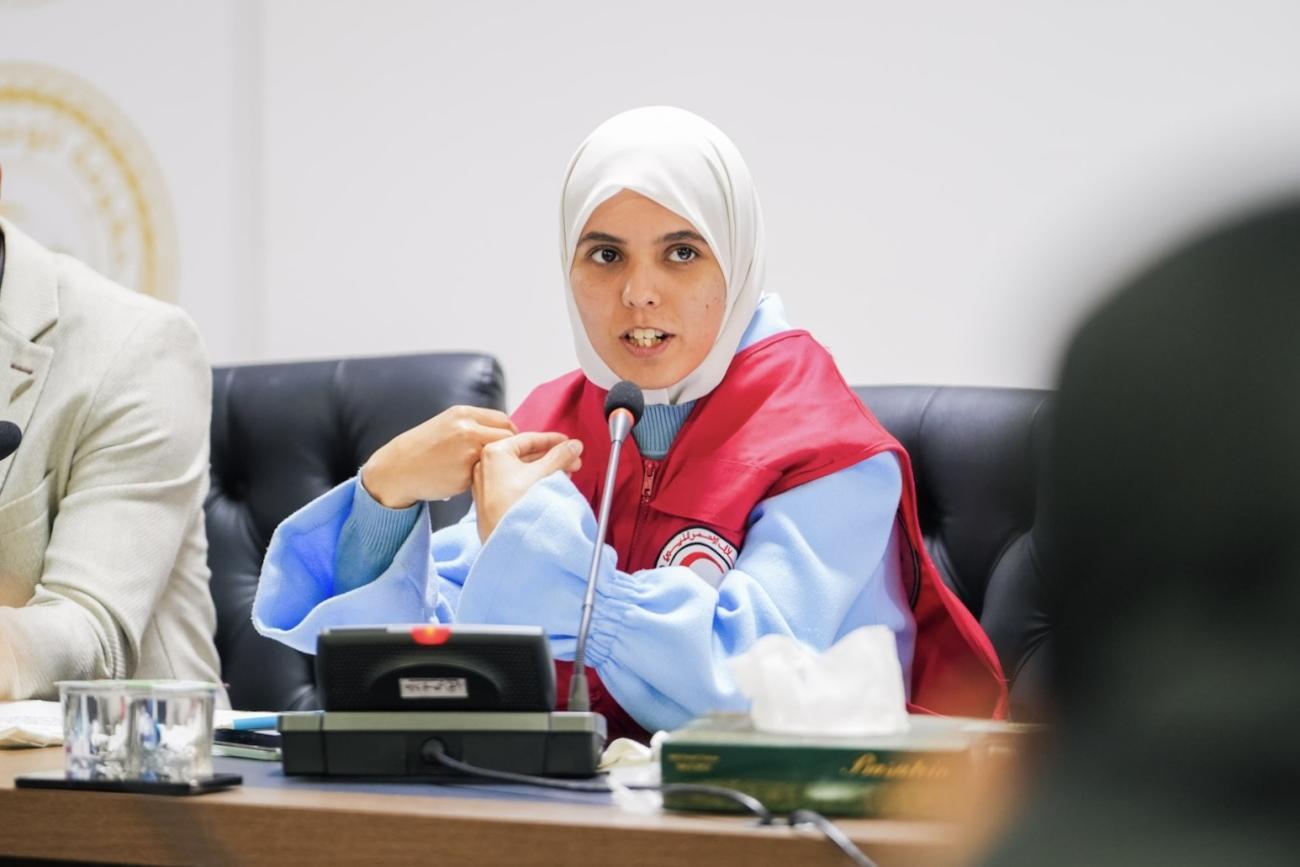 حياة، متطوّعة ترتدي سترة حمراء، تتحدث خلال اجتماع على طاولة للمؤتمرات.