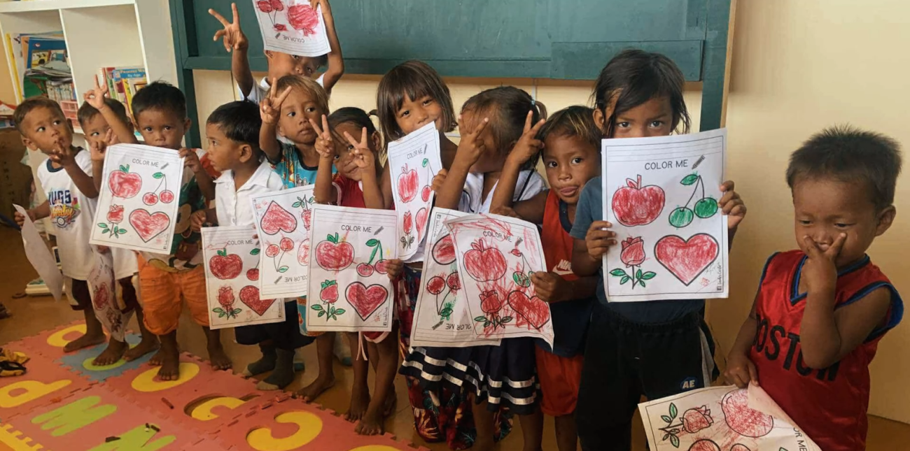 A group of children in school holding up their worksheet and making peace signs with their hands