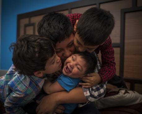 Image shows three brothers embracing and kissing their young baby brother. 