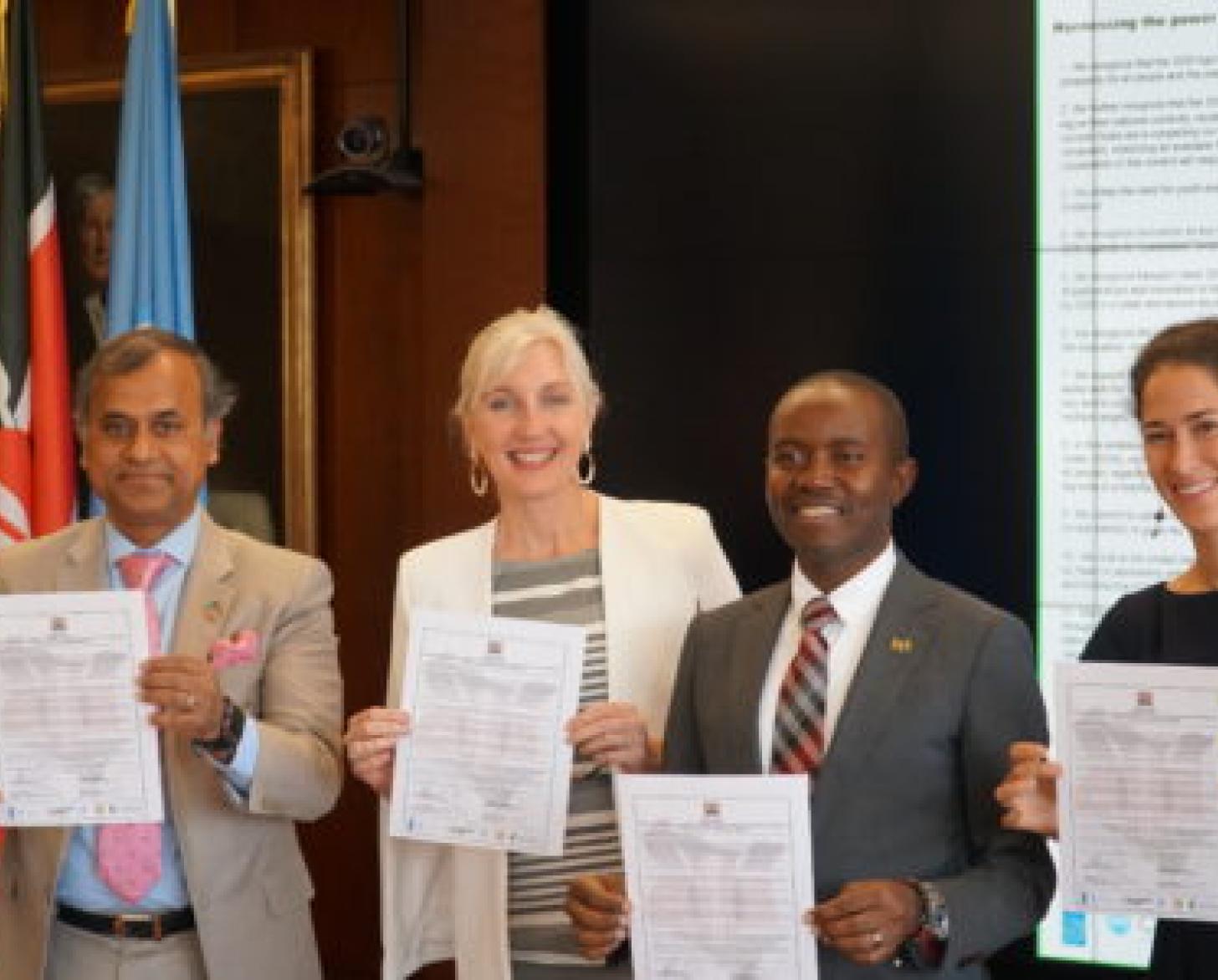 All four signatories smile as they stand holding their signed commitments