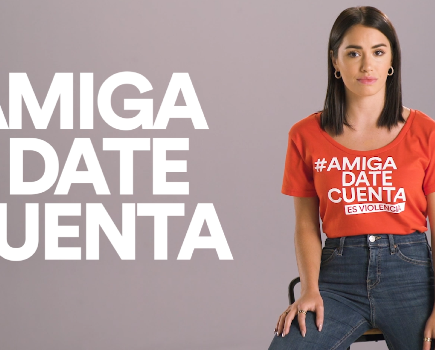 امرأة جالسة وتنظر مباشرة إلى الكاميرا وبجانبها شعر حملة باللغة الاسبانية