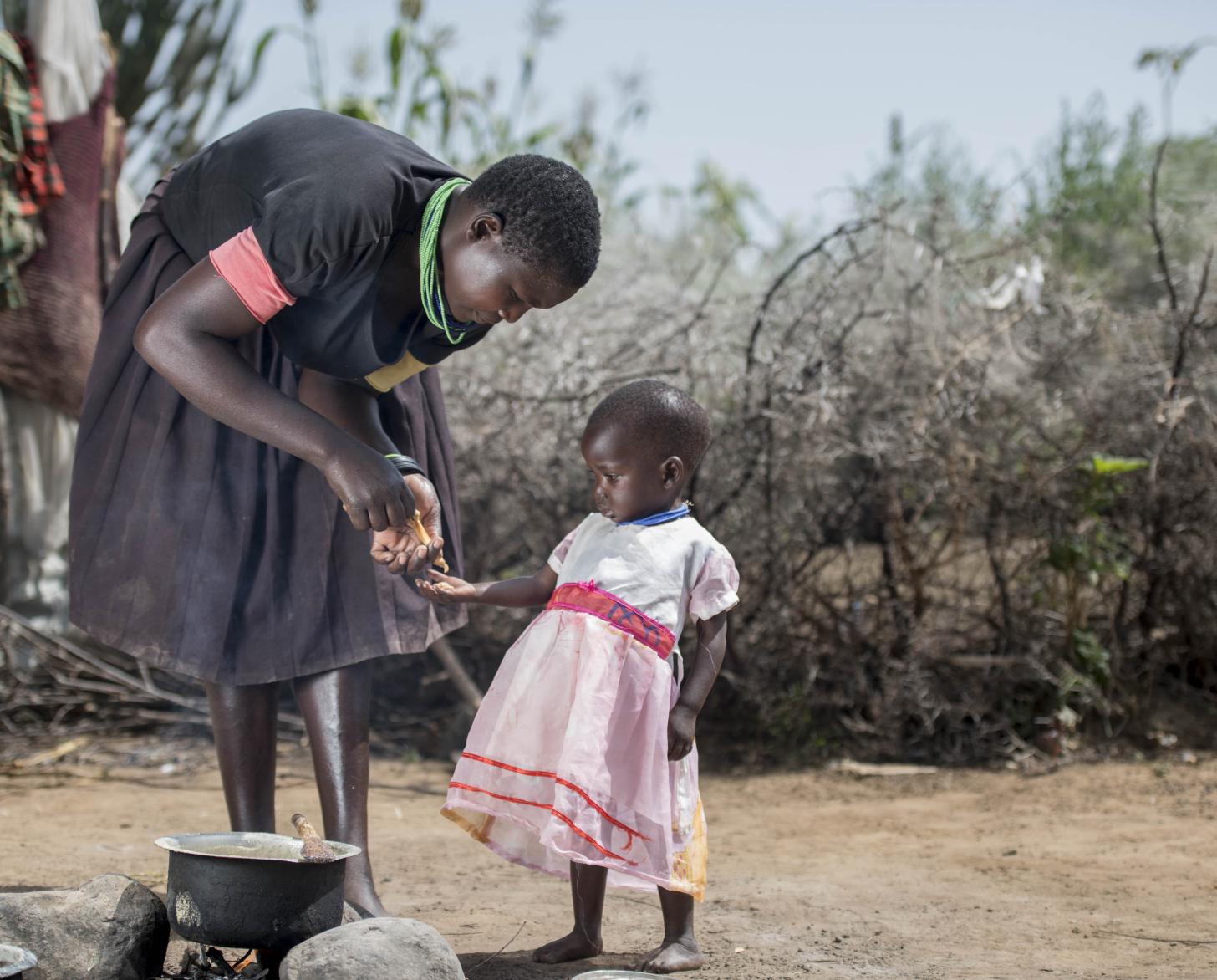 Photo shows a mother teaching her young toddler to cook.
