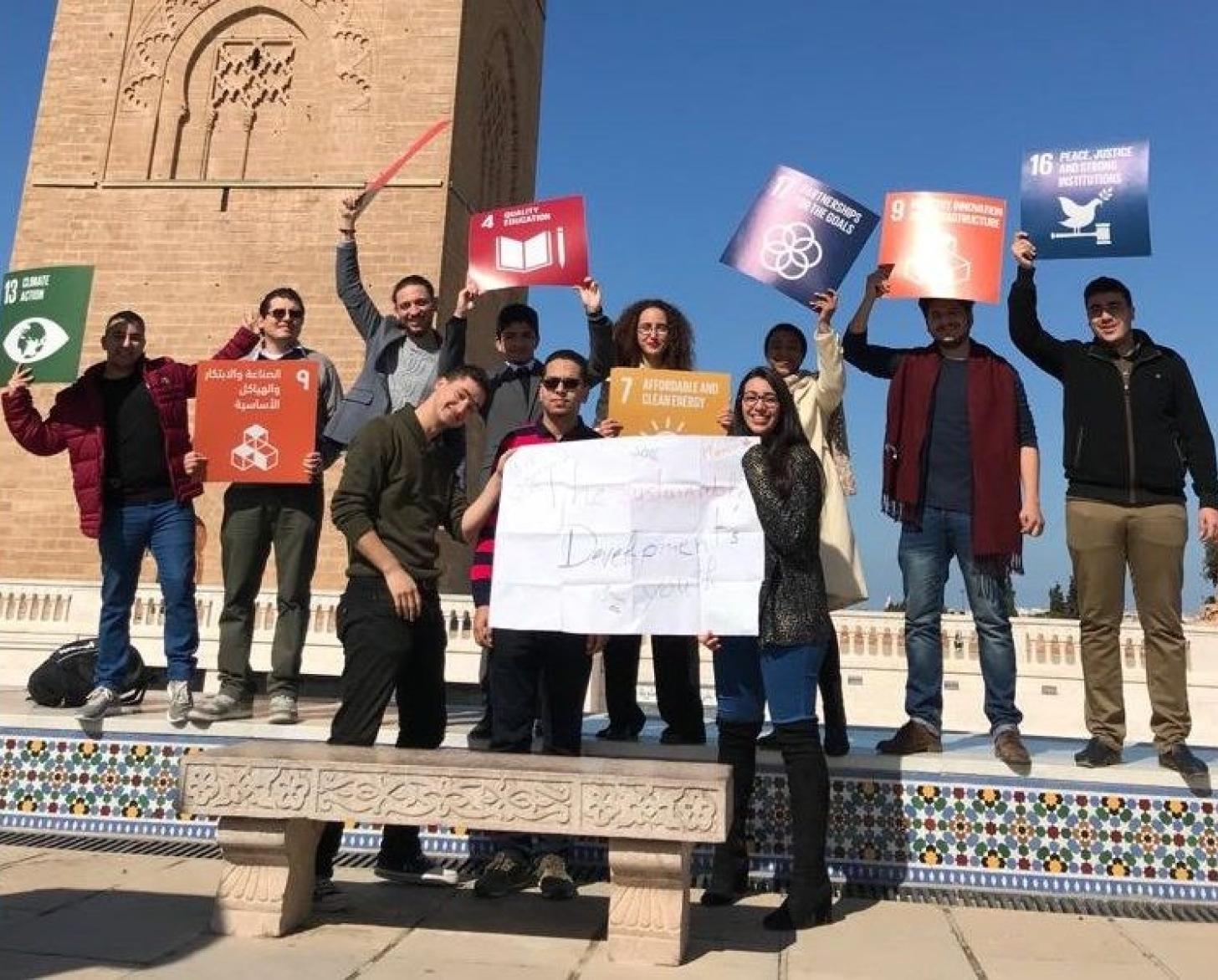 Young people pose towards the camera happily holding SDG signs.
