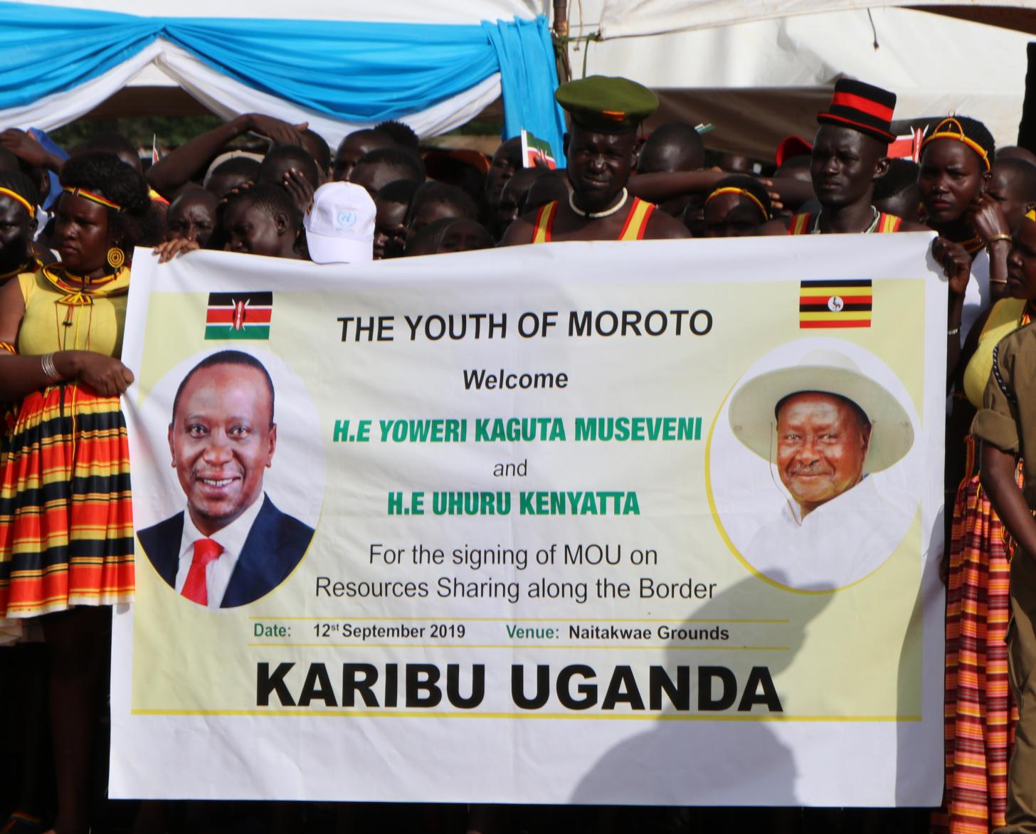 Shows a group of people holding a banner that shows heads of Kenya and Uganda.