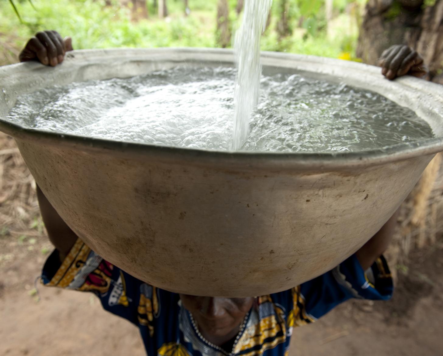 La mujer sostiene un recipiente de metal grande en la cabeza, mientras el mismo se llena de agua.