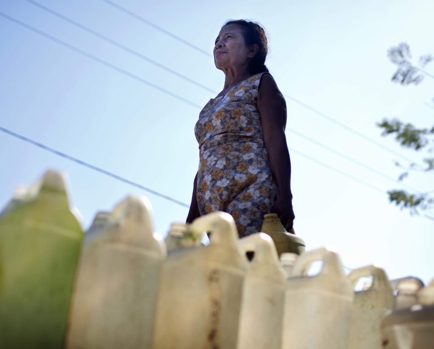 Woman walks passed jugs of water on the ground.