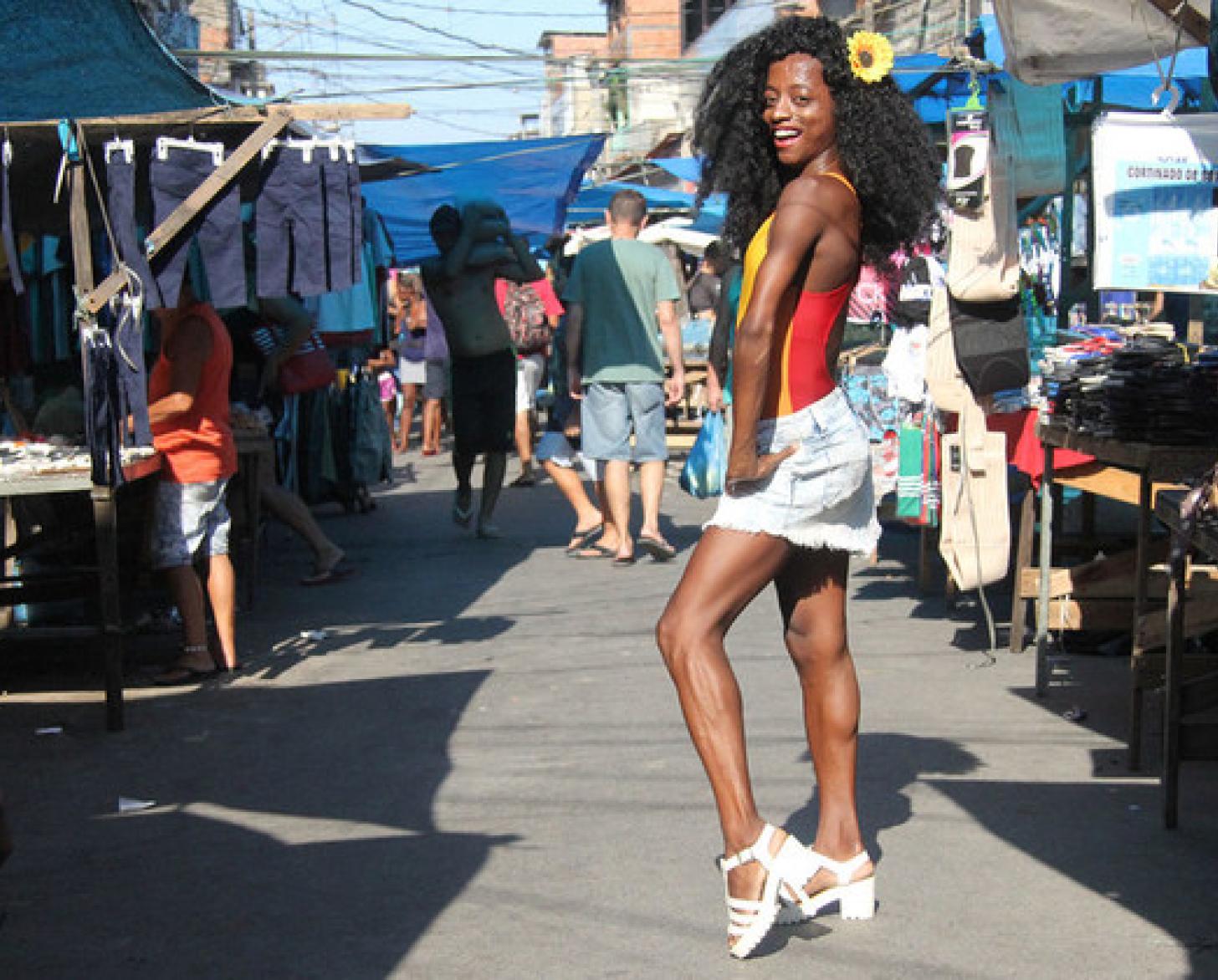 Shows young person smiling and posing at the camera, while at a local market.