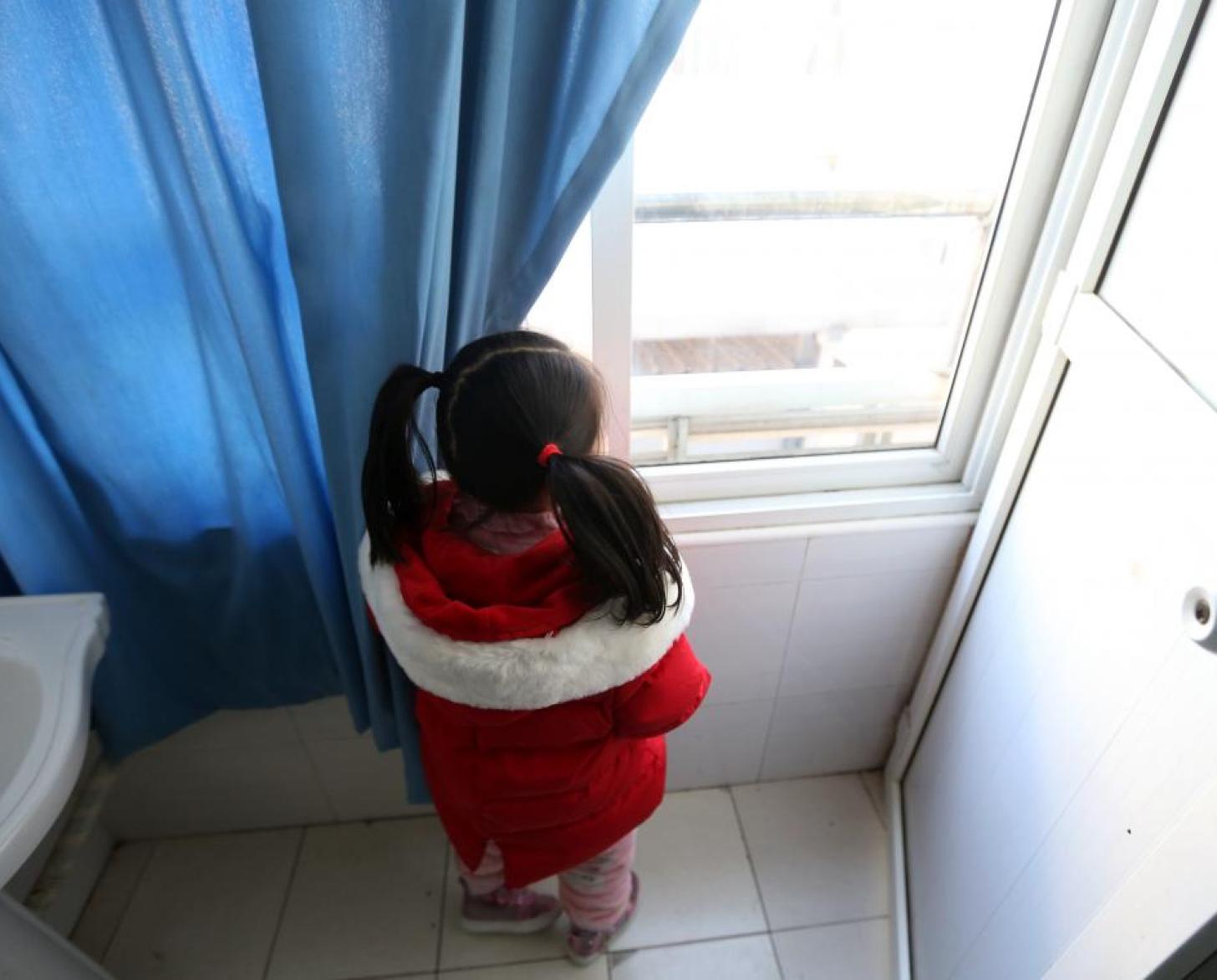 Niña pequeña observando por la ventana.