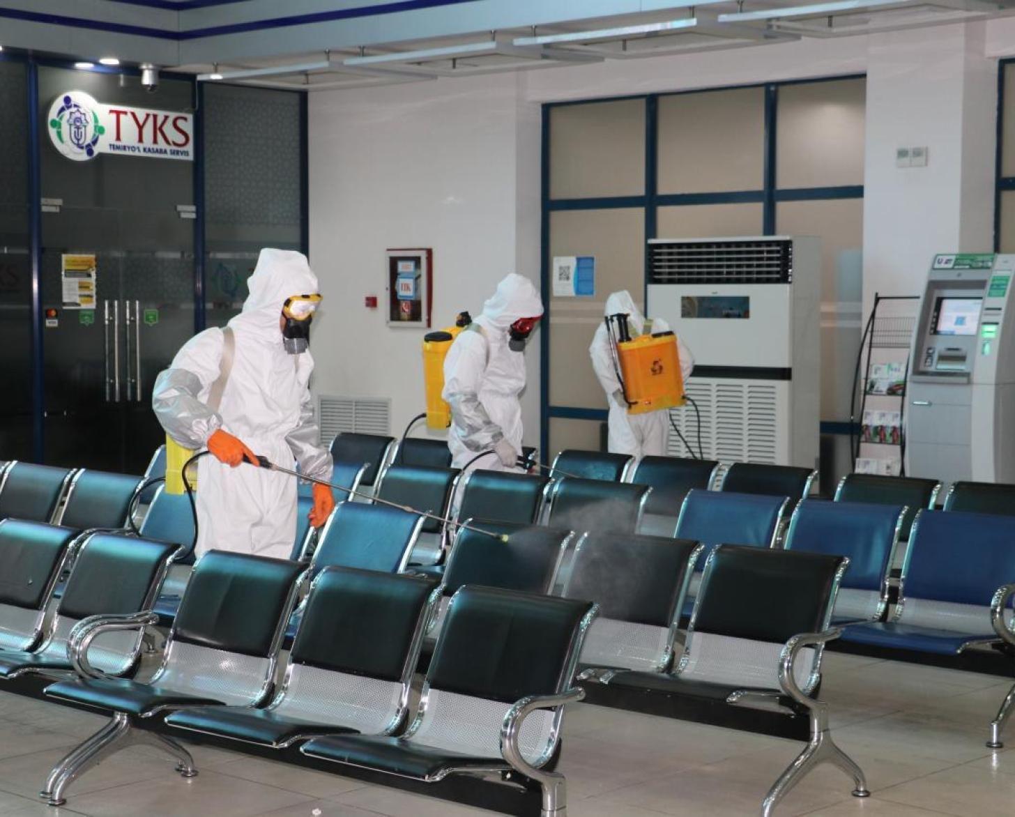 Se muestra a personas que usan equipo de protección de la cabeza a los pies limpiando y desinfectando un área de espera.