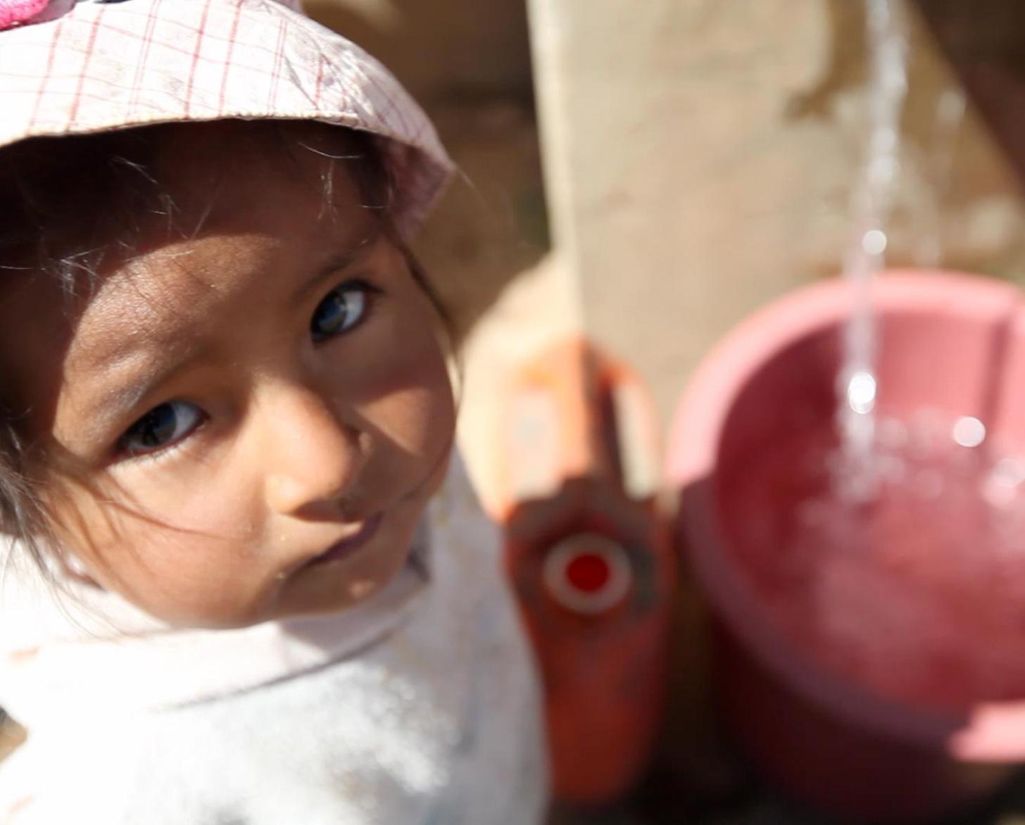 Little girl looks at the camera as water fills her container.