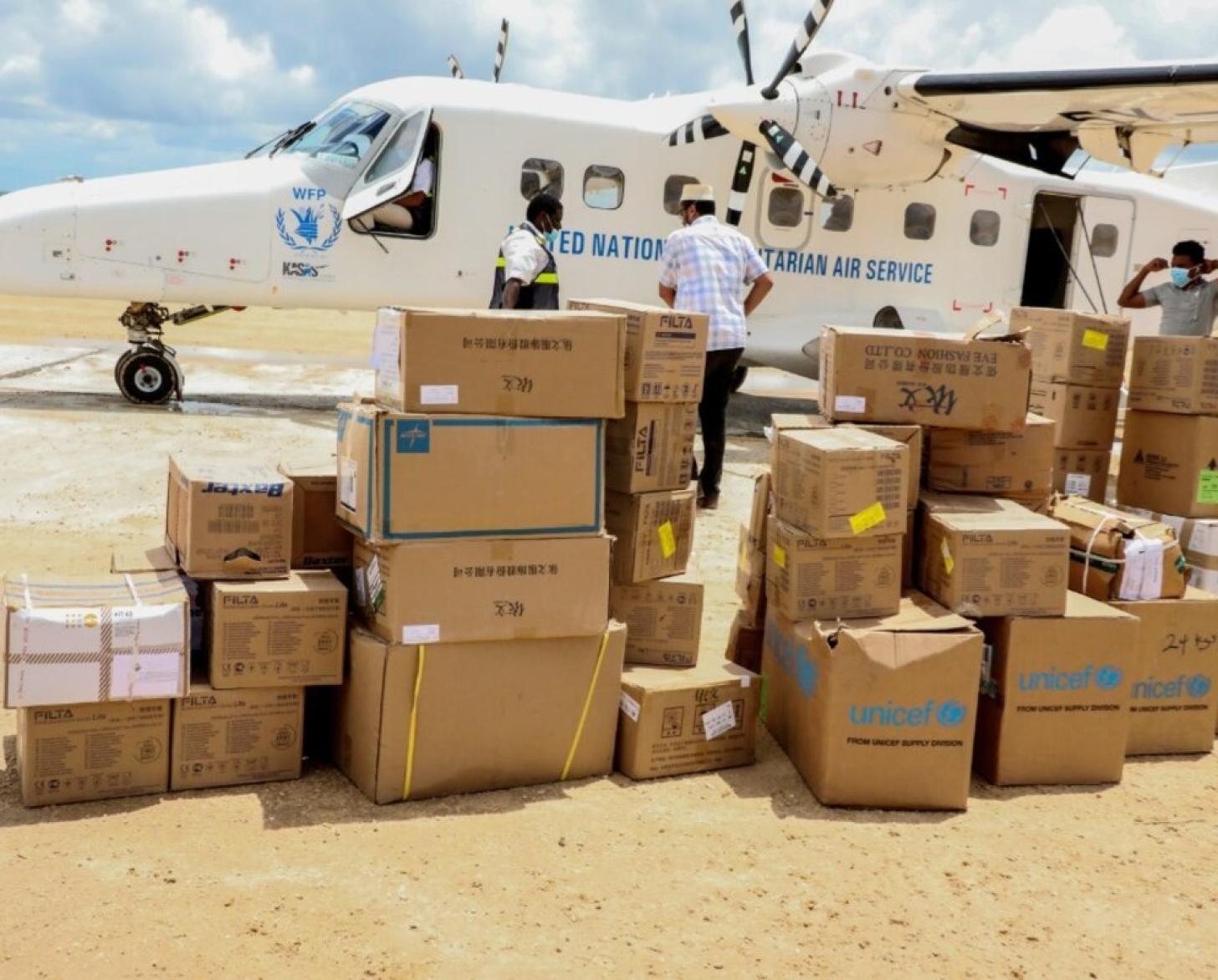 An aircraft with the WFP emblem is shown with boxes of supplies in the foreground.