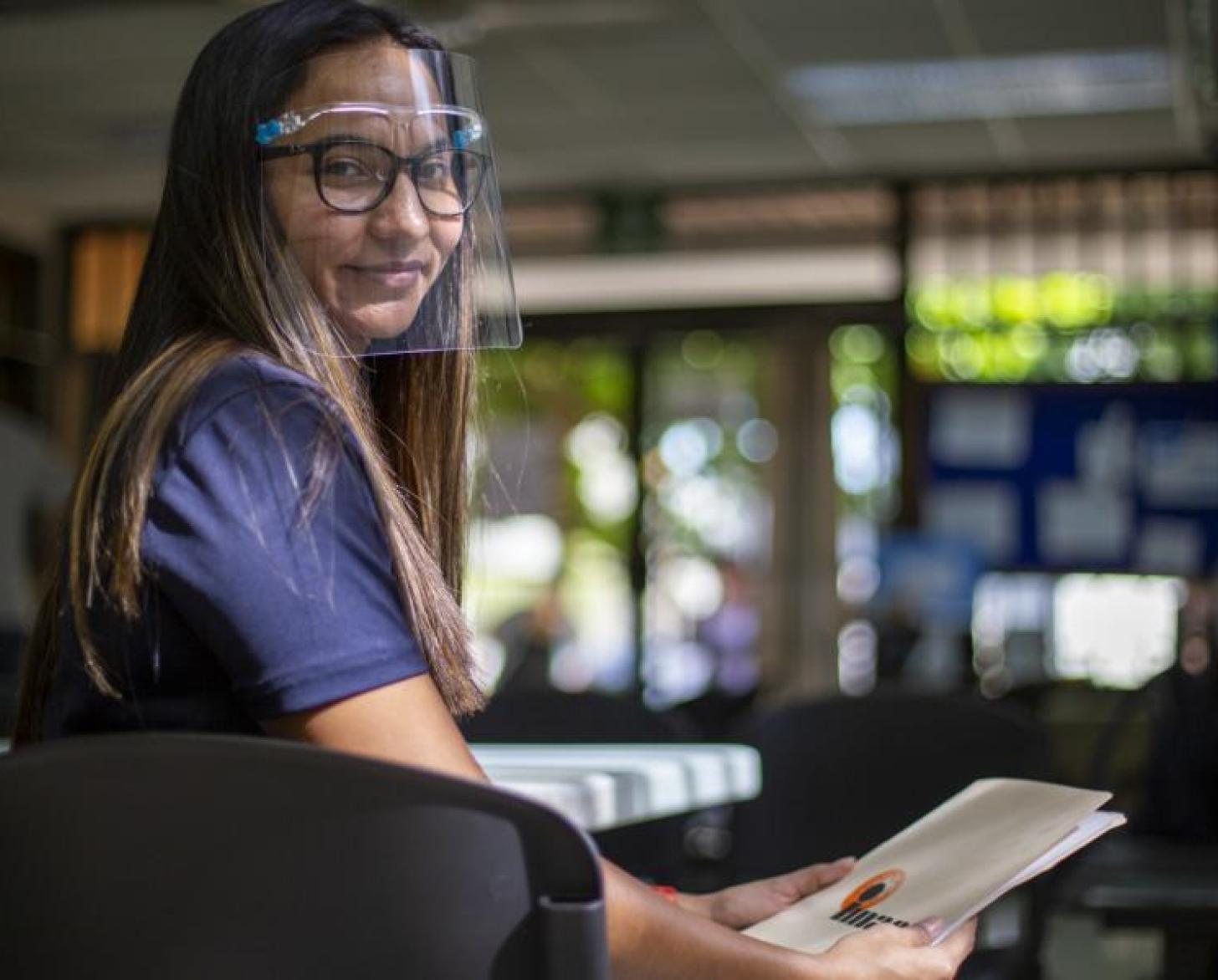 Gabriela smiles proudly at the camera as she holds a folder of material for her clients.