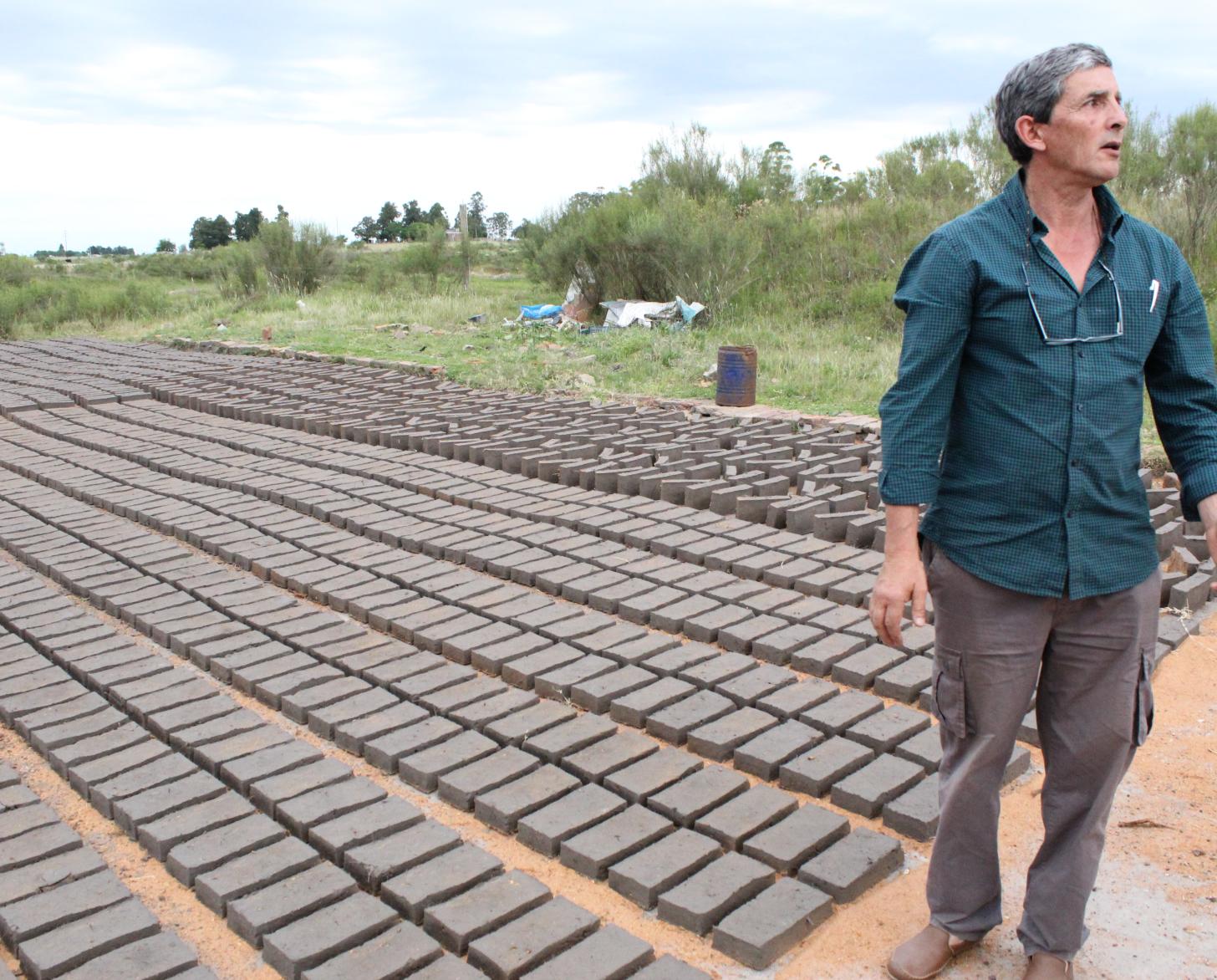 Eduard Romero stands in front of the bricks spread across the ground set under the sun to dry.