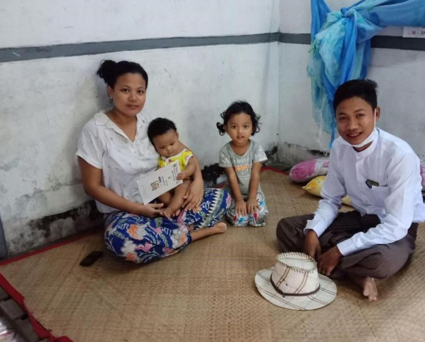 A woman sits with her children and husband on the floor of their residence.