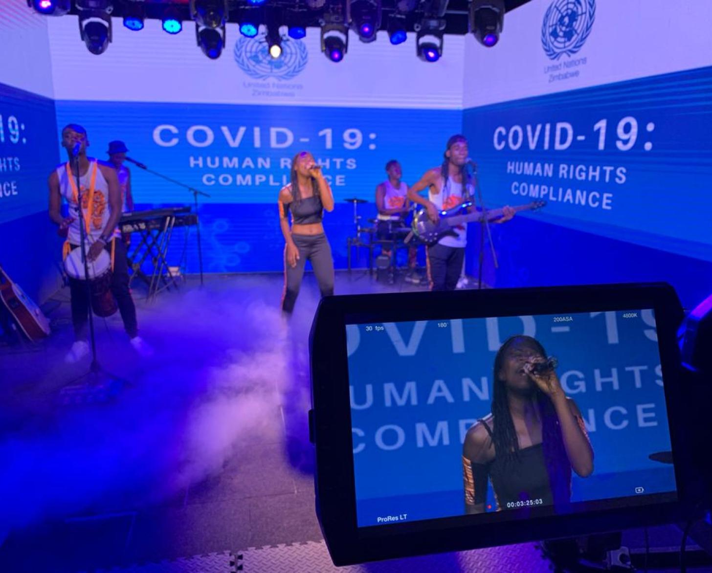 Caroleen Masawi and her band perform surrounded by green screens featuring a COVID-19 message.