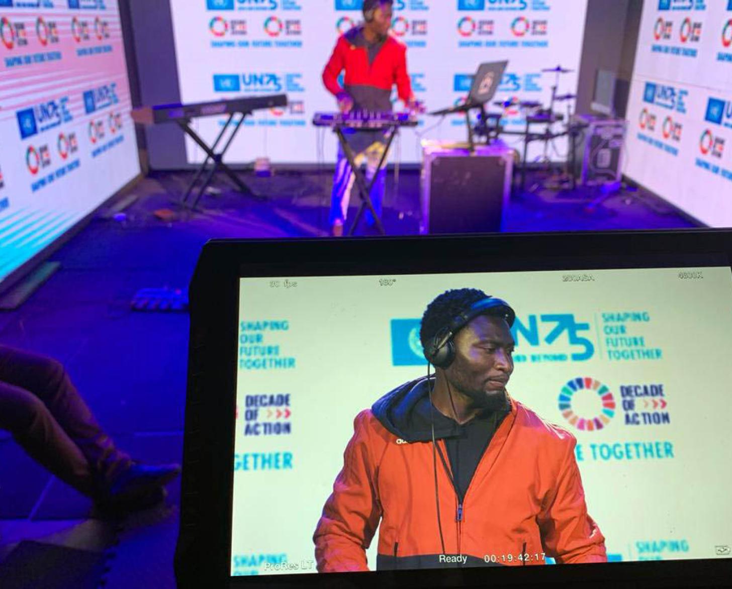 DJ Yayos performs while being recorded. The photo shows him in the background with an image of him on an screen in the foreground.