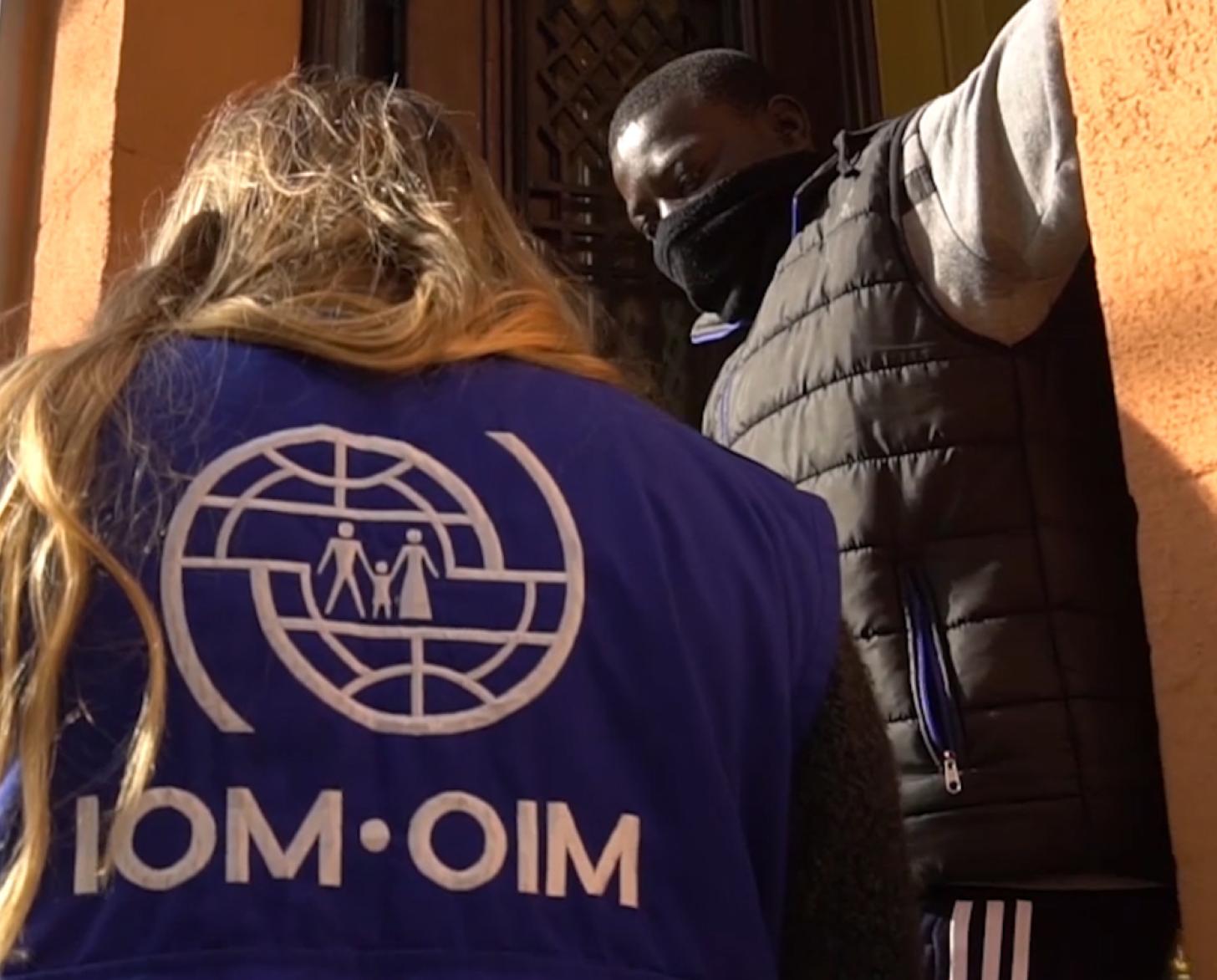 An IOM Staff speaks to a man at the entry to his home.