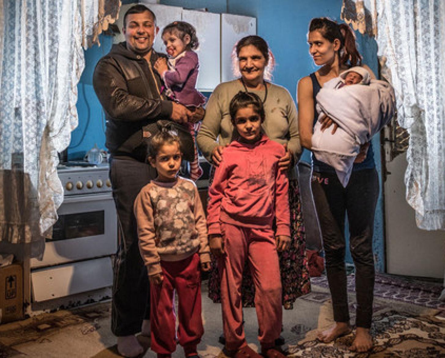 A Roma family smiles happily as they stand together in their home in Belgrade.
