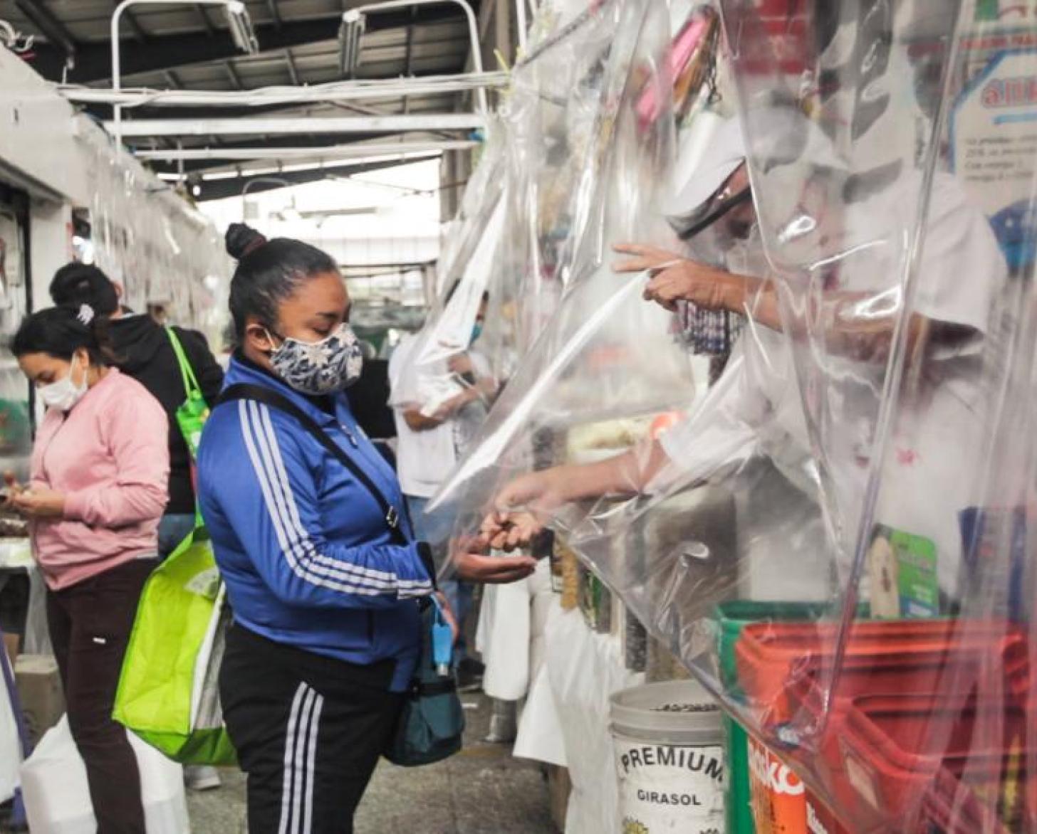 A vendor behind a clear plastic shield provides change to one of his customers.