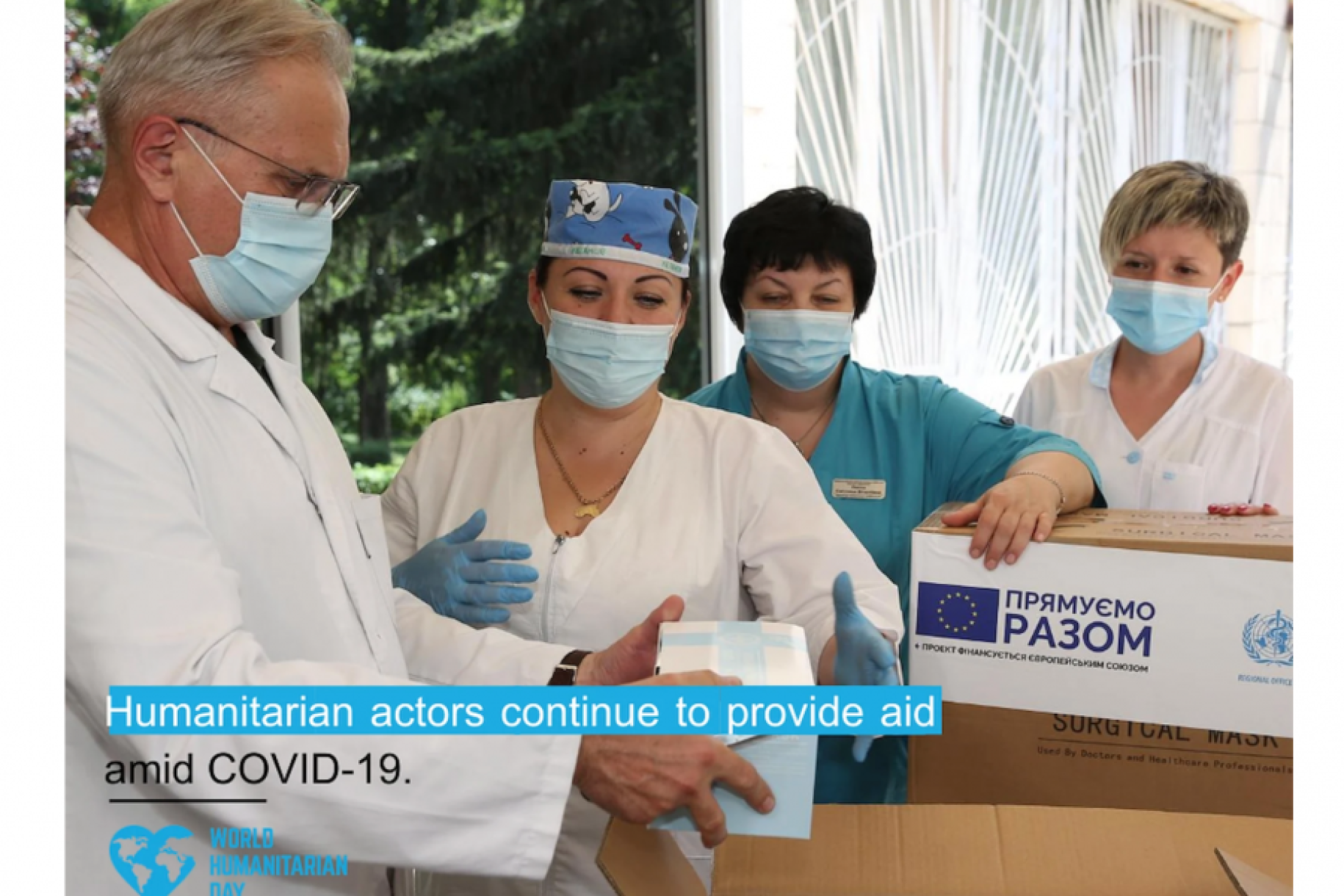 Un trabajador sanitario abre cajas de donaciones con artículos de primera necesidad con el texto "Las acciones humanitarias continúan proporcionando ayuda en medio de la COVID-19".