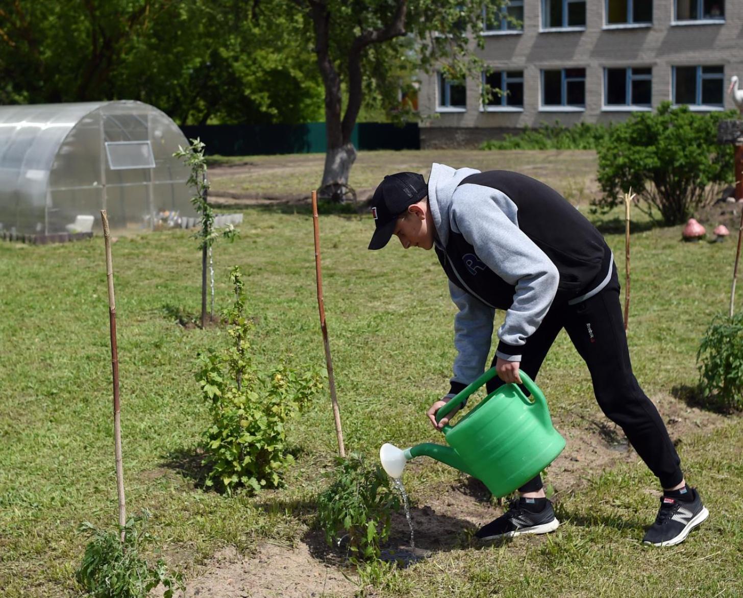 Un joven riega las plantas fuera de la escuela.