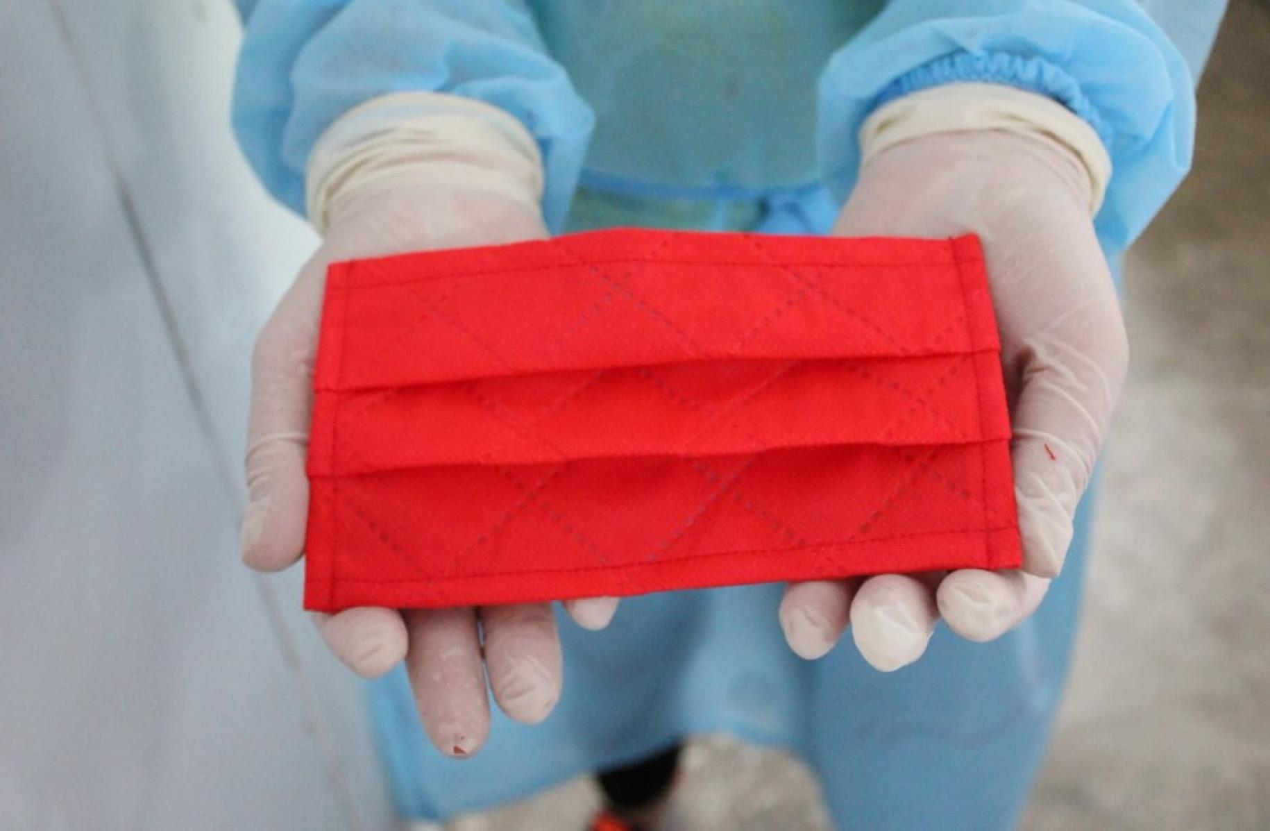 Un primer plano de las dos manos de una persona con guantes blancos sosteniendo una máscara protectora roja.
