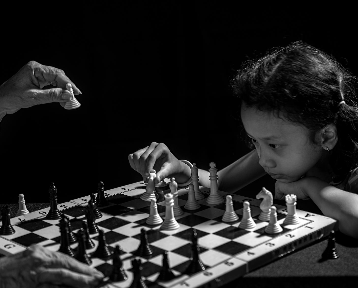 Black and white photo of a young girl puzzling out her next move in a game of chess with her grandmother.