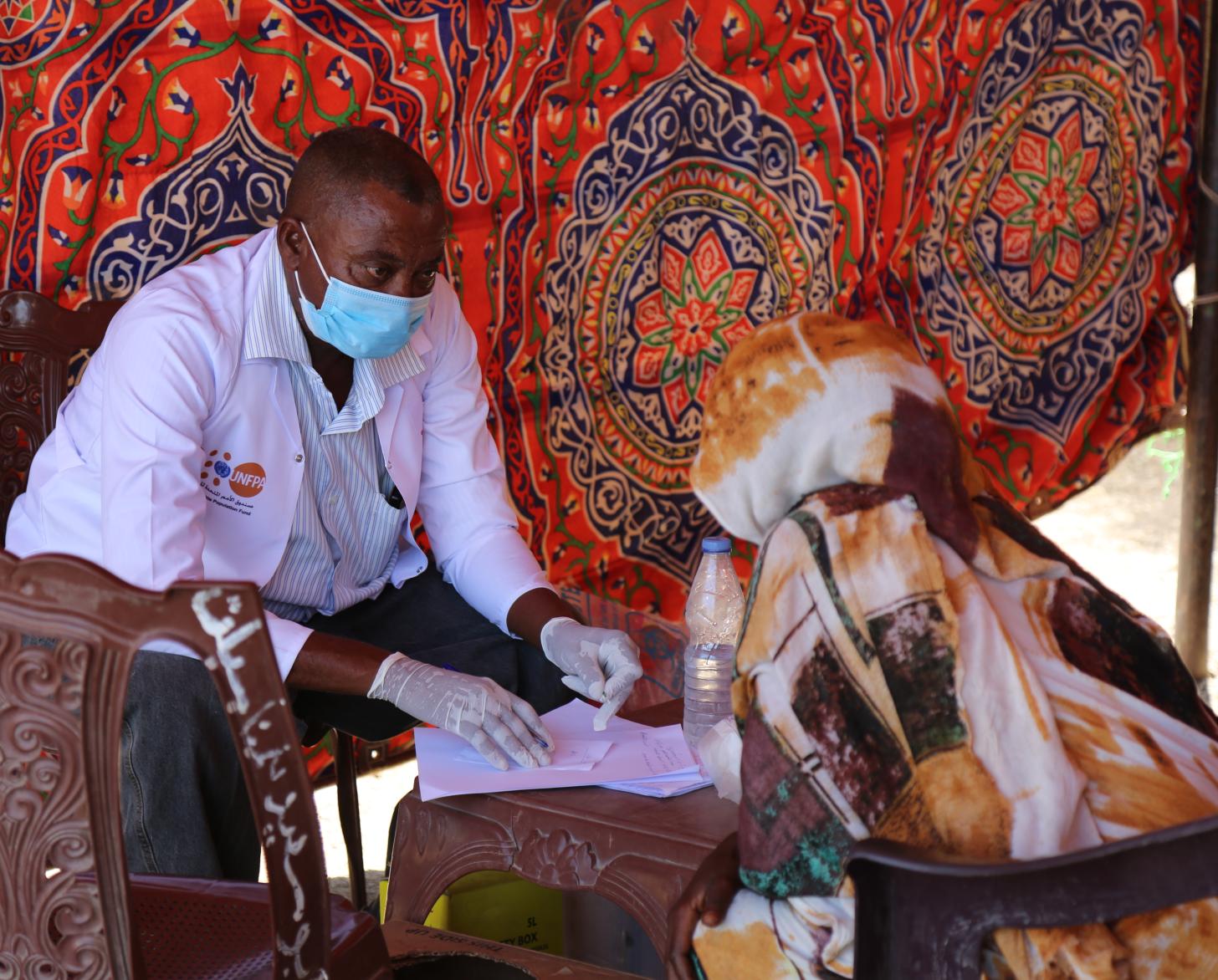 A healthcare professional sits with a patient in a tent at the camp.