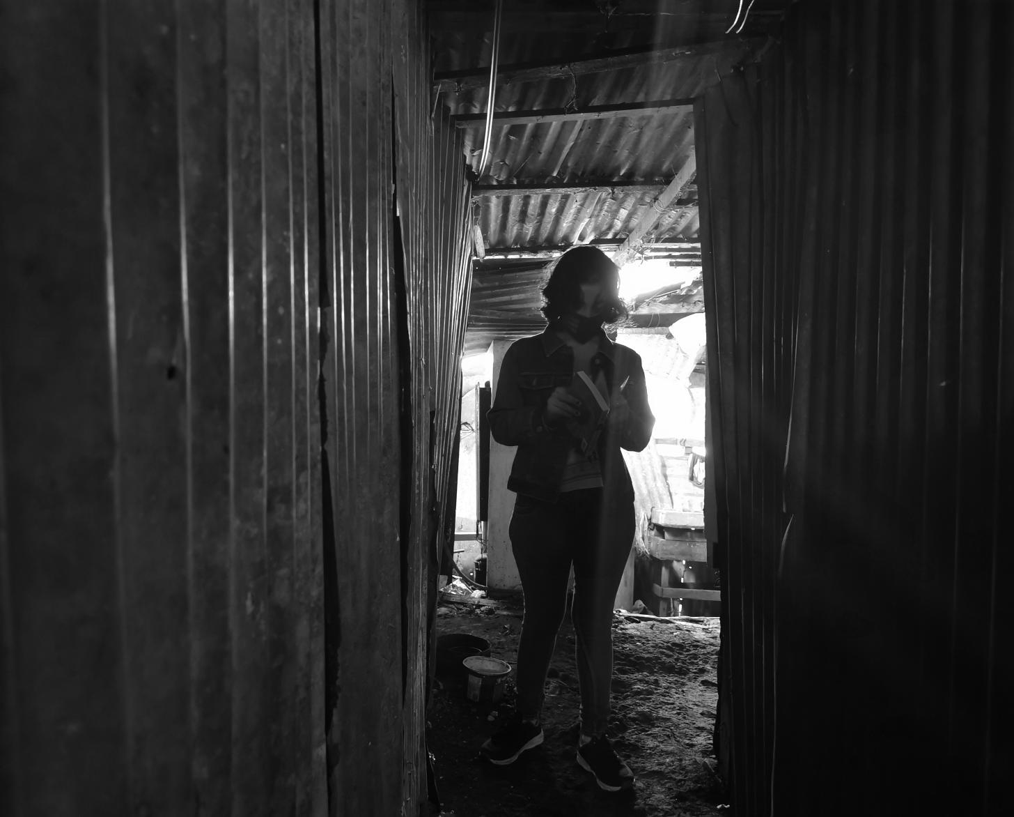 Lilith stands at the end of a passageway as she looks down at her book.