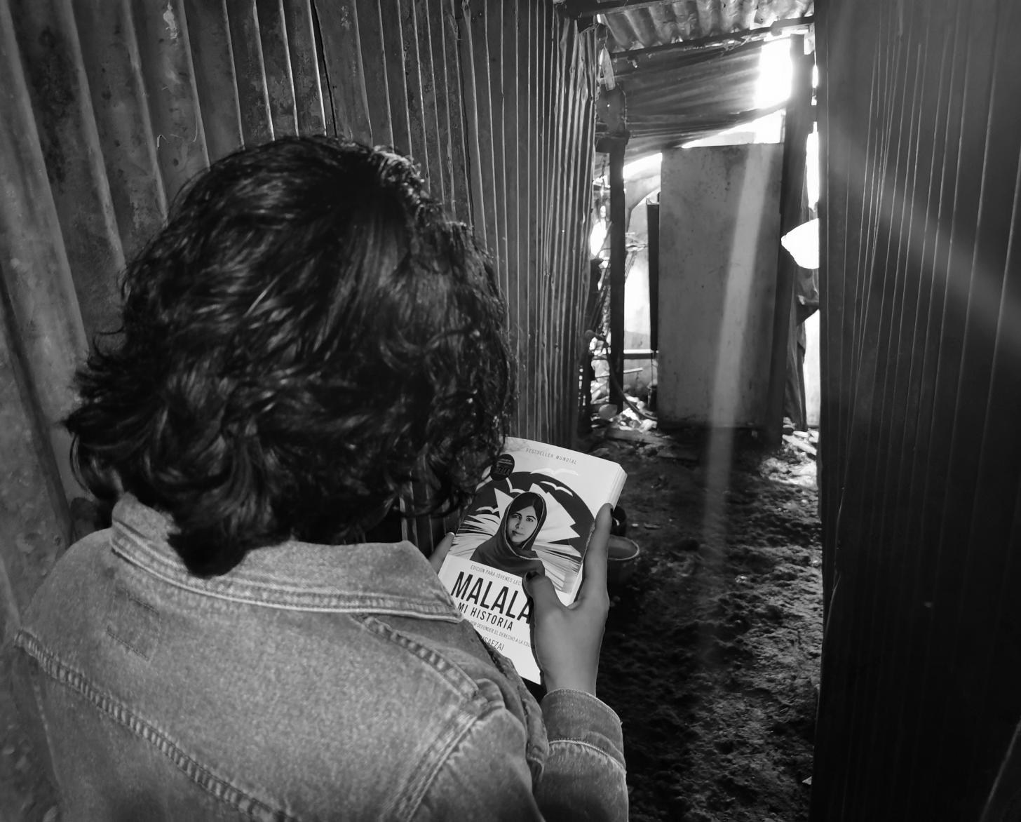 Lilith turns away from the camera and stares at Malala's book, which she holds in front of her.