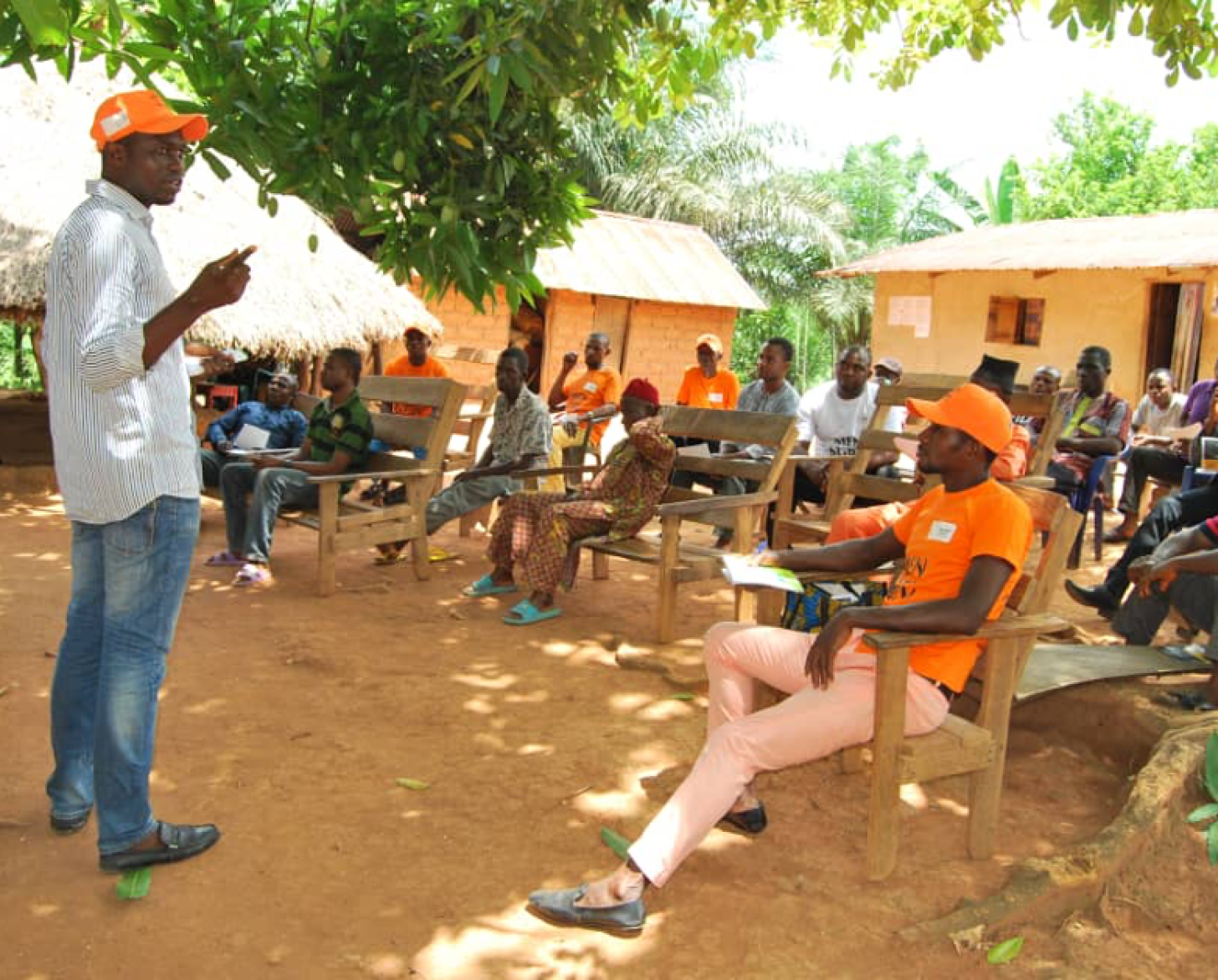 Clement stands in front of a group of men seated as he presents to them issues related to gender-based violence. 