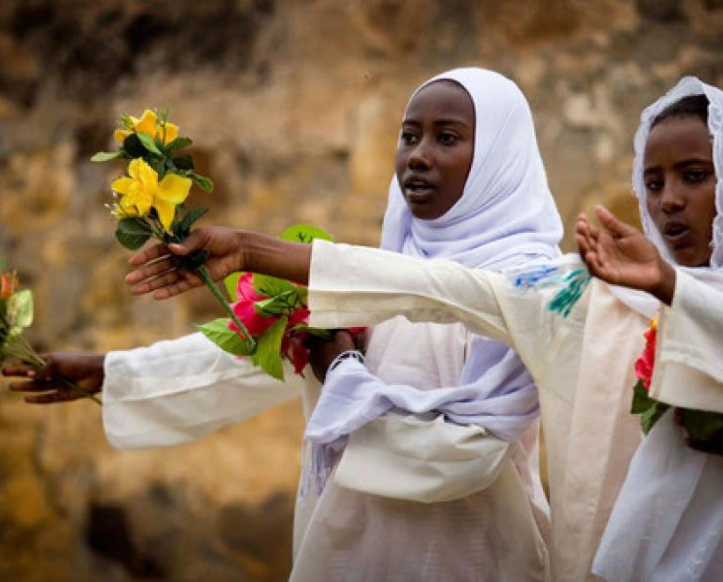 Dos adolescentes con velo blanco aparecen extendiendo sus manos con flores.