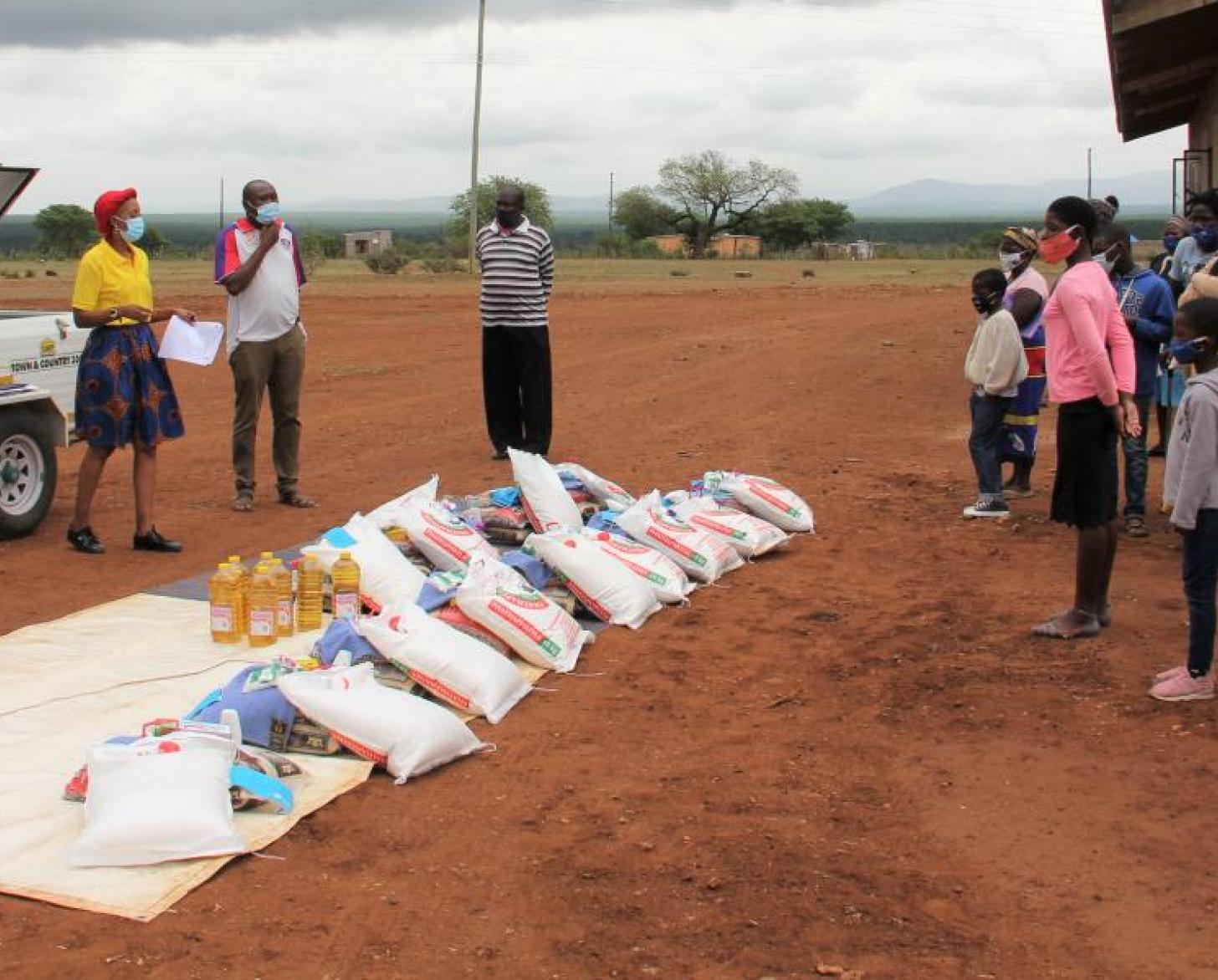 UN staff and families, wearing face masks, all stand outside on the opposite sides of a row of supplies placed in the middle.