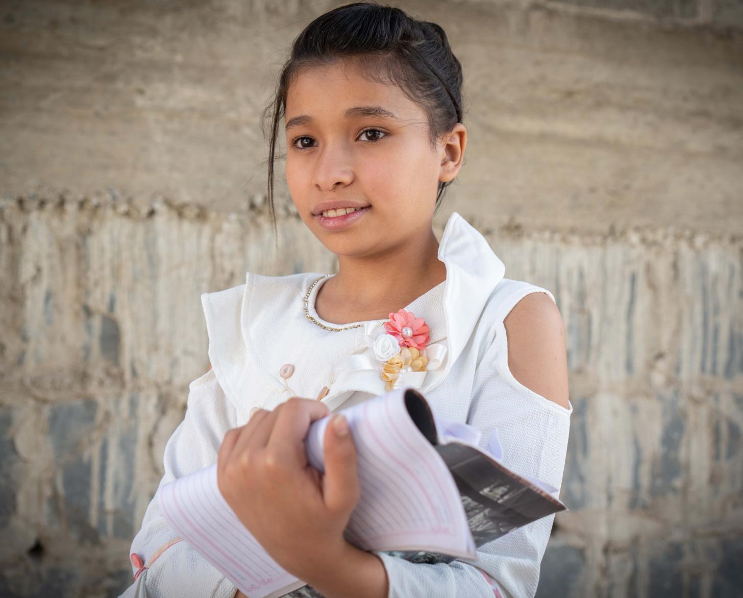 12-year-old Amina looks off the camera as she proudly holds her notebook.