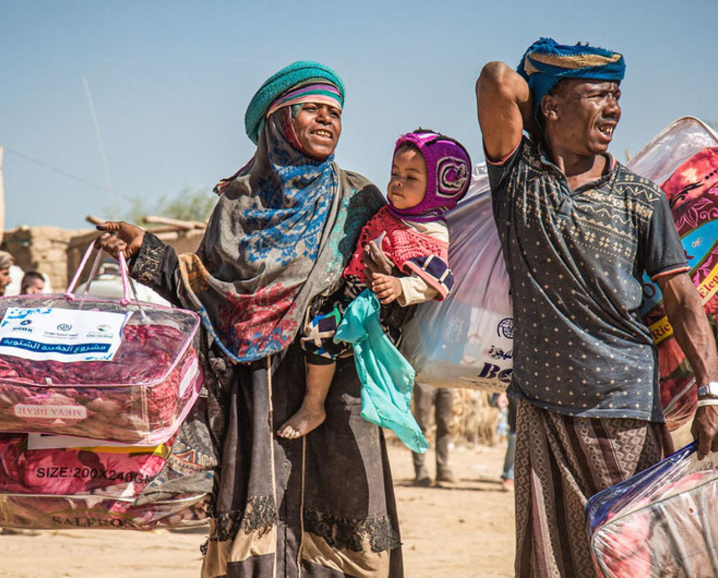 A displaced family in Marib, Yemen, carries a winter aid package back to their shelter.